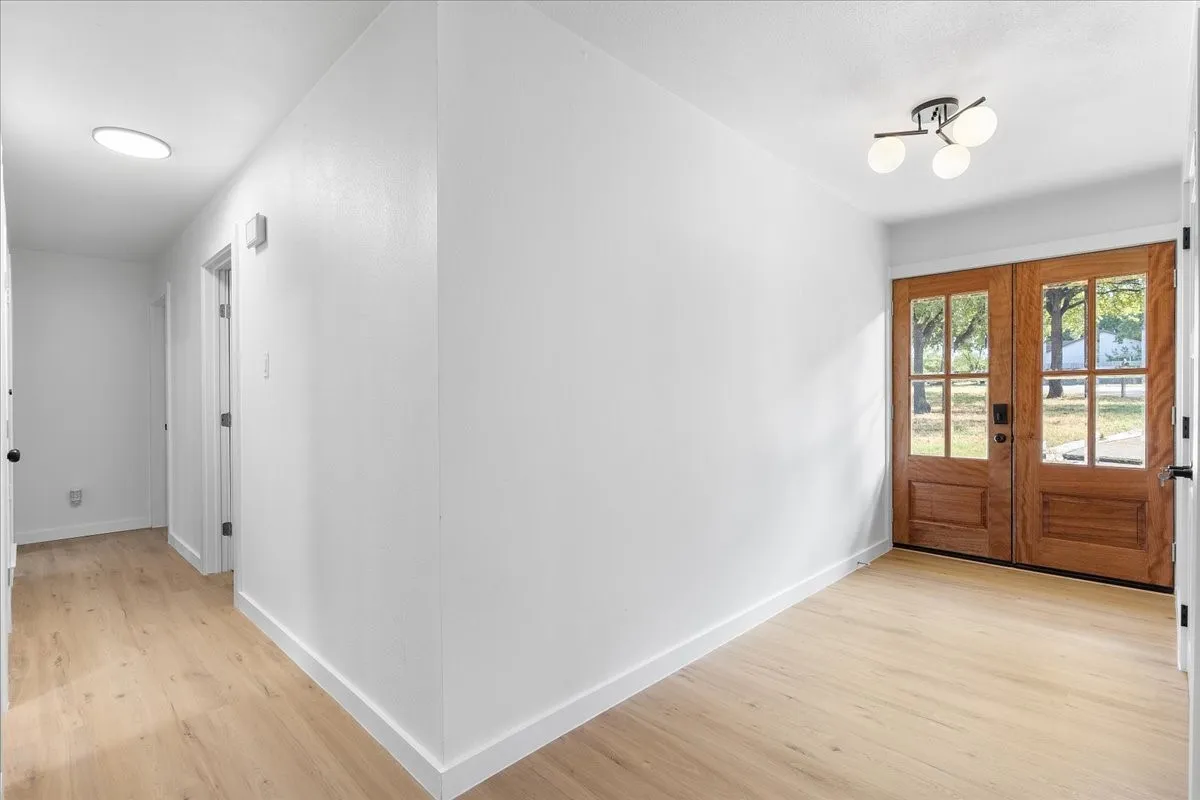 Wood-finish flooring throughout, bright white walls, modern ceiling light fixture, and wood-paneled double entry doors with glass lites