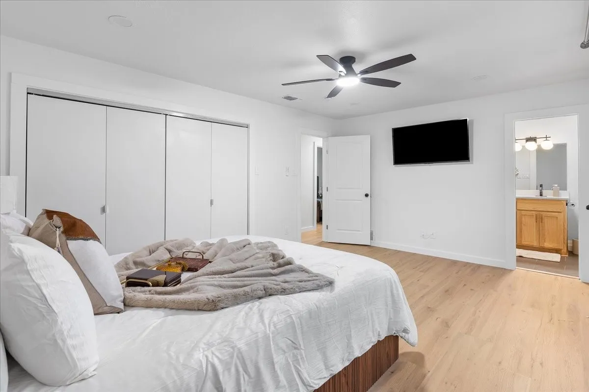 Wood-finish flooring, ceiling fan with integrated lighting, built-in closet with sliding doors, and a full bathroom featuring a wood-finish vanity