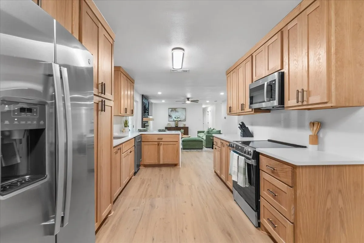 Galley kitchen featuring wood cabinetry, stainless steel appliances, white countertops, wood-finish flooring, and recessed lighting
