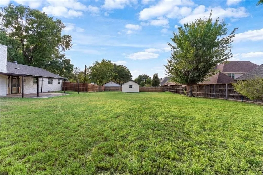 Expansive grass lawn with a covered patio, wood fencing, and a detached storage shed