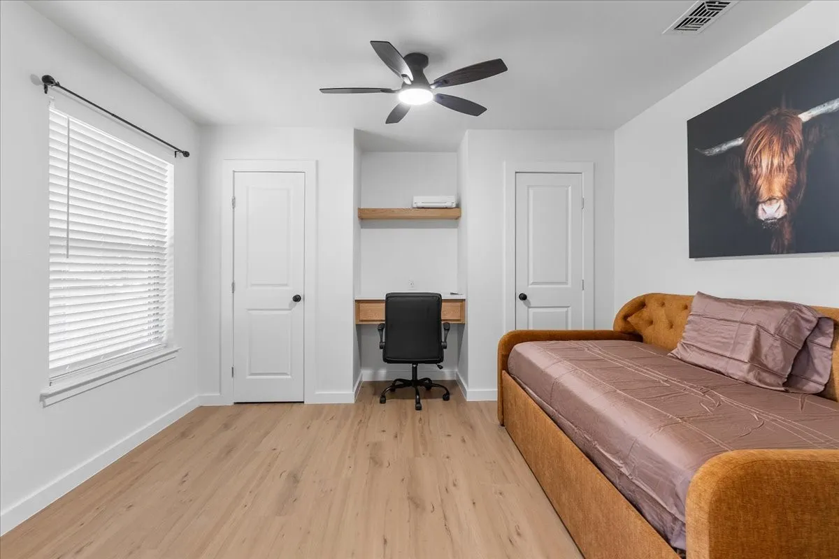 Great Flex room. Use as Bedroom or Office! Double Modern Doors, Recessed desk area with a wood-finish shelf, wood-finish flooring, and a ceiling fan with integrated lighting