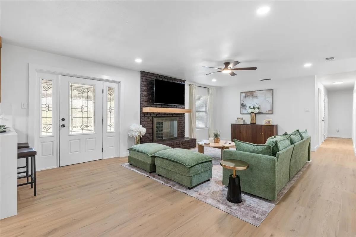 Spacious living area featuring wood-finish flooring, a brick fireplace with a wood mantle, and an entry door with decorative glass inserts
