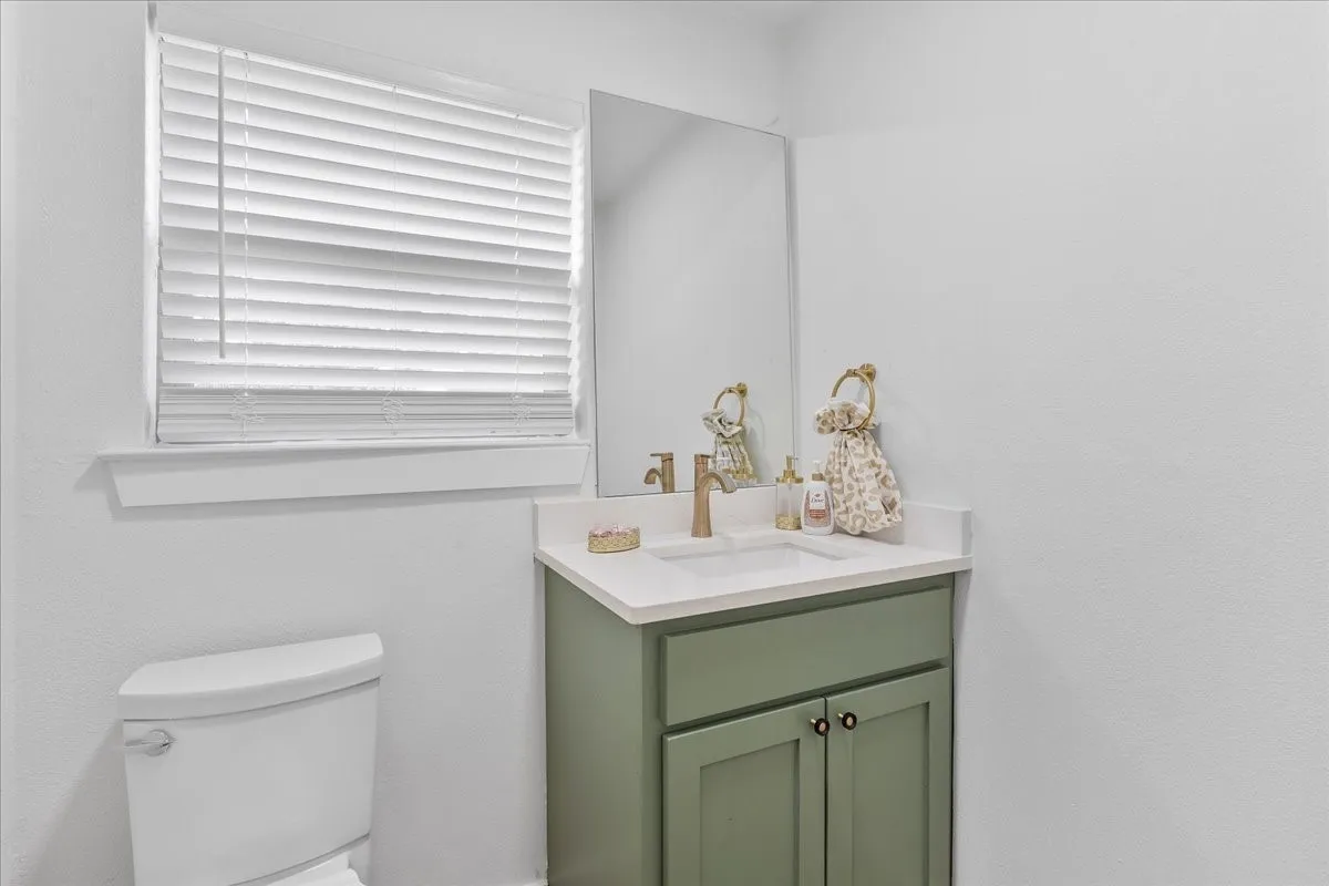 White wall-mounted toilet, vanity with sage green cabinetry, white countertop, integrated sink, and a rectangular mirror