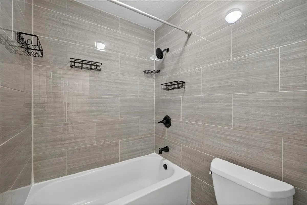 Bathtub with matte black fixtures, light gray large format tile surround, and recessed lighting
