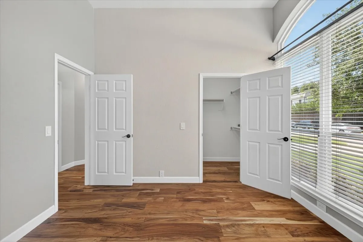 Wood-finish flooring, vaulted ceilings, arched window, built-in shelving, and neutral wall tones