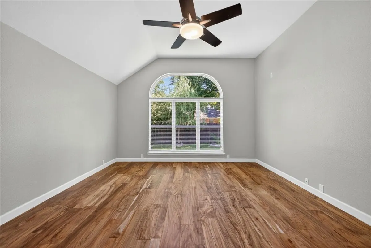 Vaulted ceiling with a ceiling fan, arched window, wood-finish flooring, and light-toned wall finishes