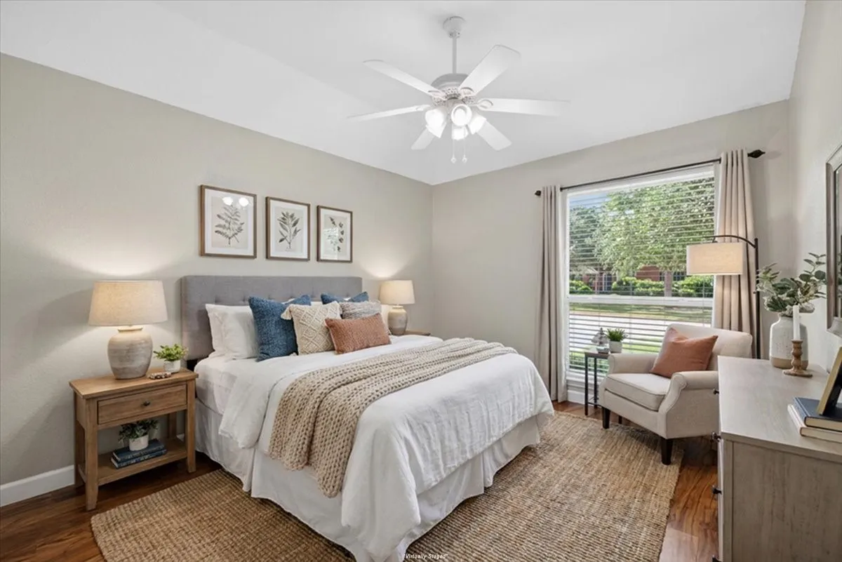 Hardwood-finish flooring, large window with blinds, ceiling fan with integrated lighting, neutral wall tones, and an upholstered headboard