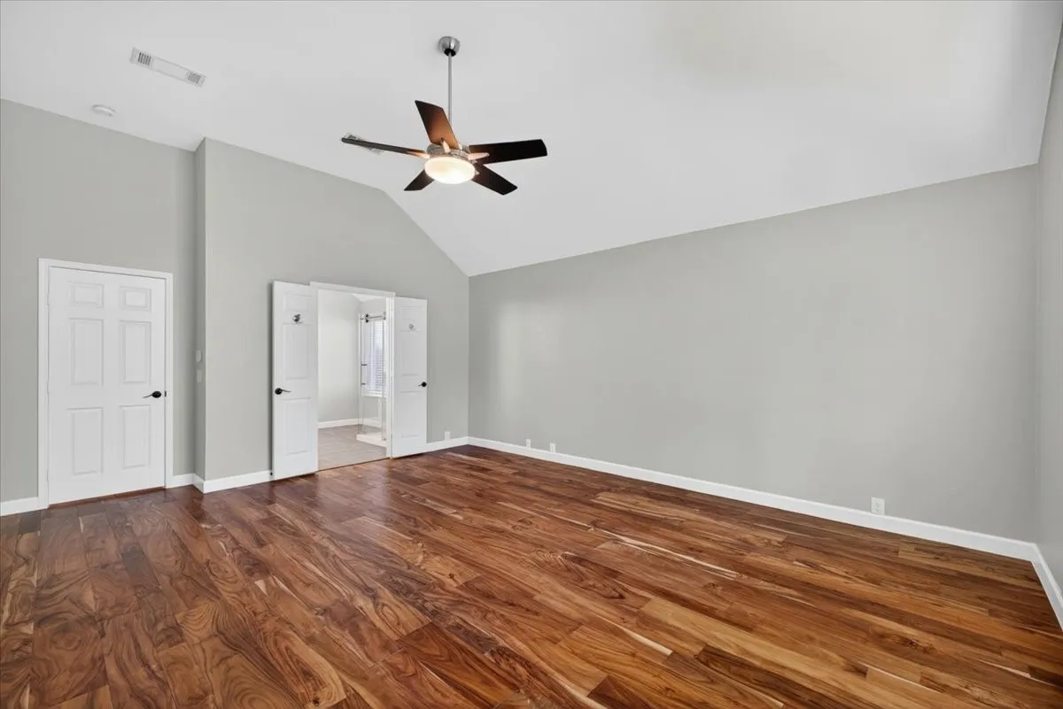 Vaulted ceiling with a ceiling fan, wood-finish flooring, light gray wall paint, and white paneled doors