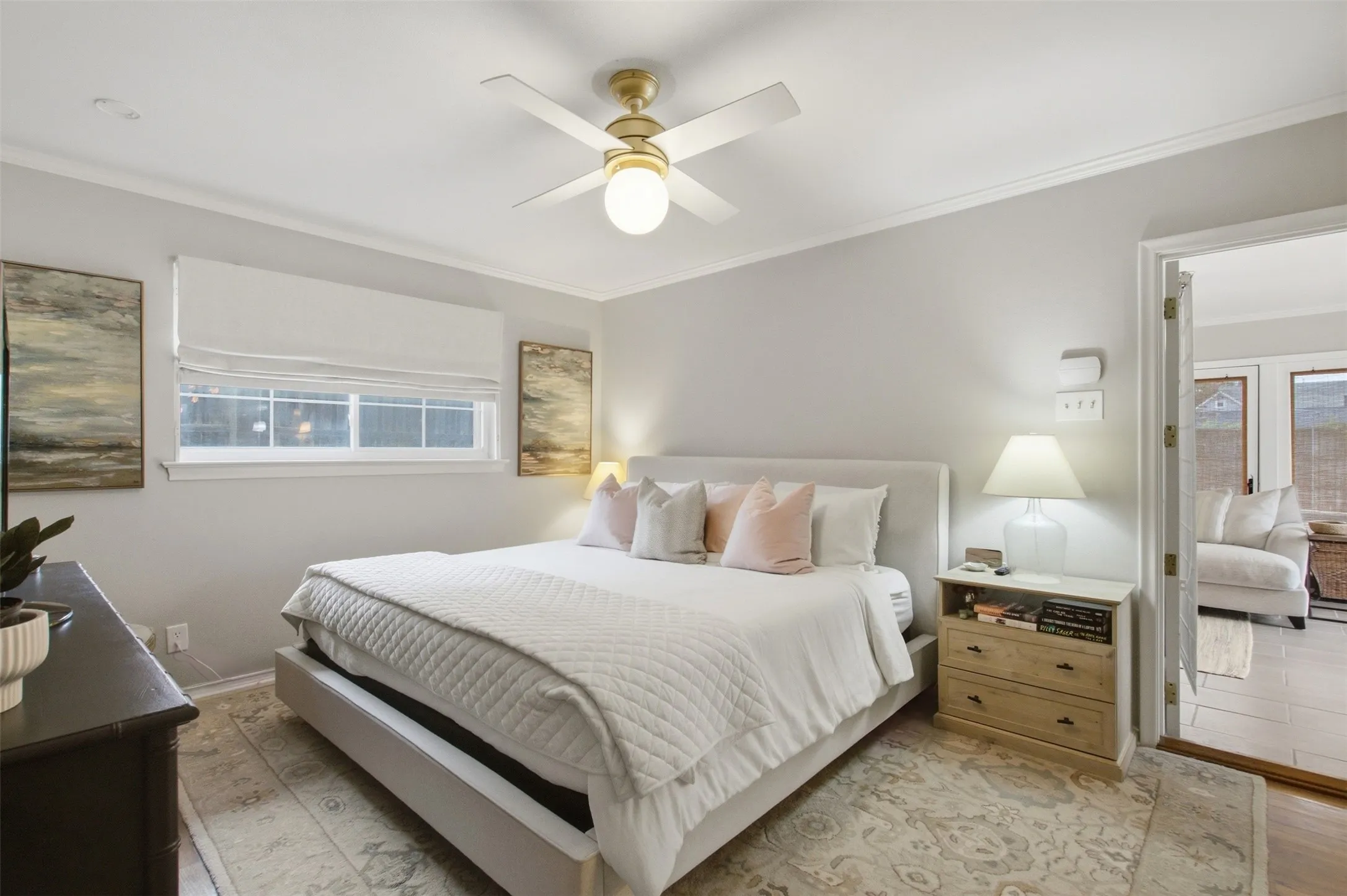 Light-filled interior featuring a ceiling fan with integrated lighting, wood-finish flooring, and a window with a Roman shade