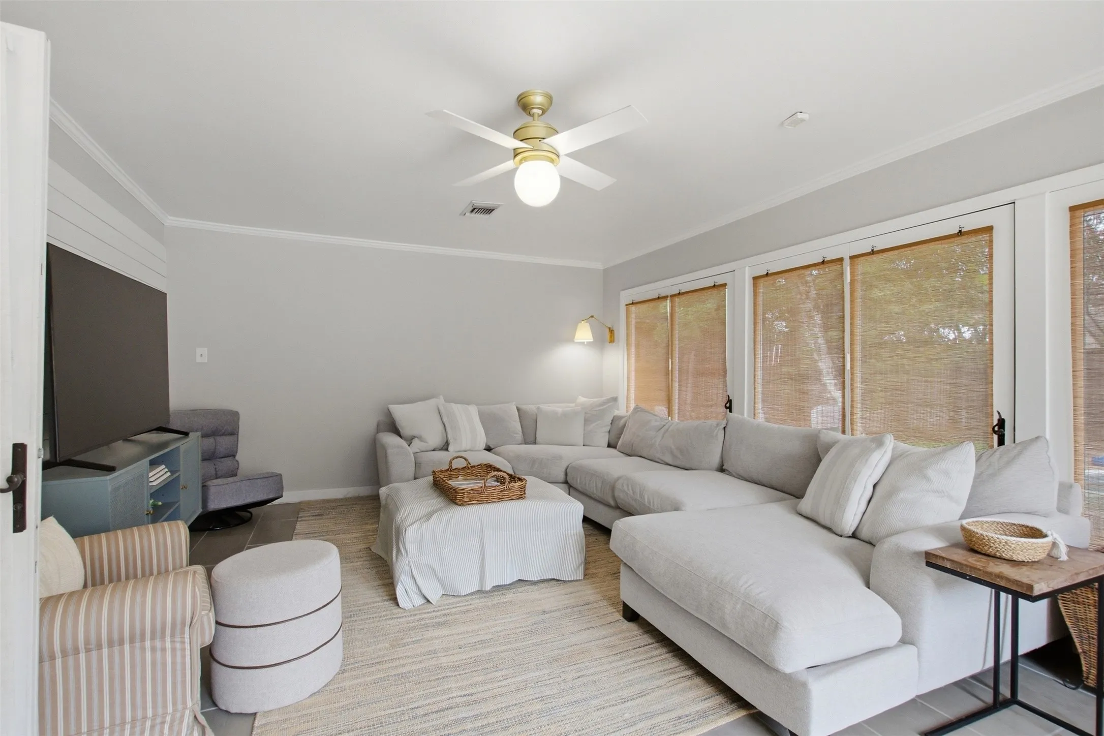 Spacious living area featuring light gray walls, crown molding, a ceiling fan with integrated lighting, and multiple windows with natural wood blinds