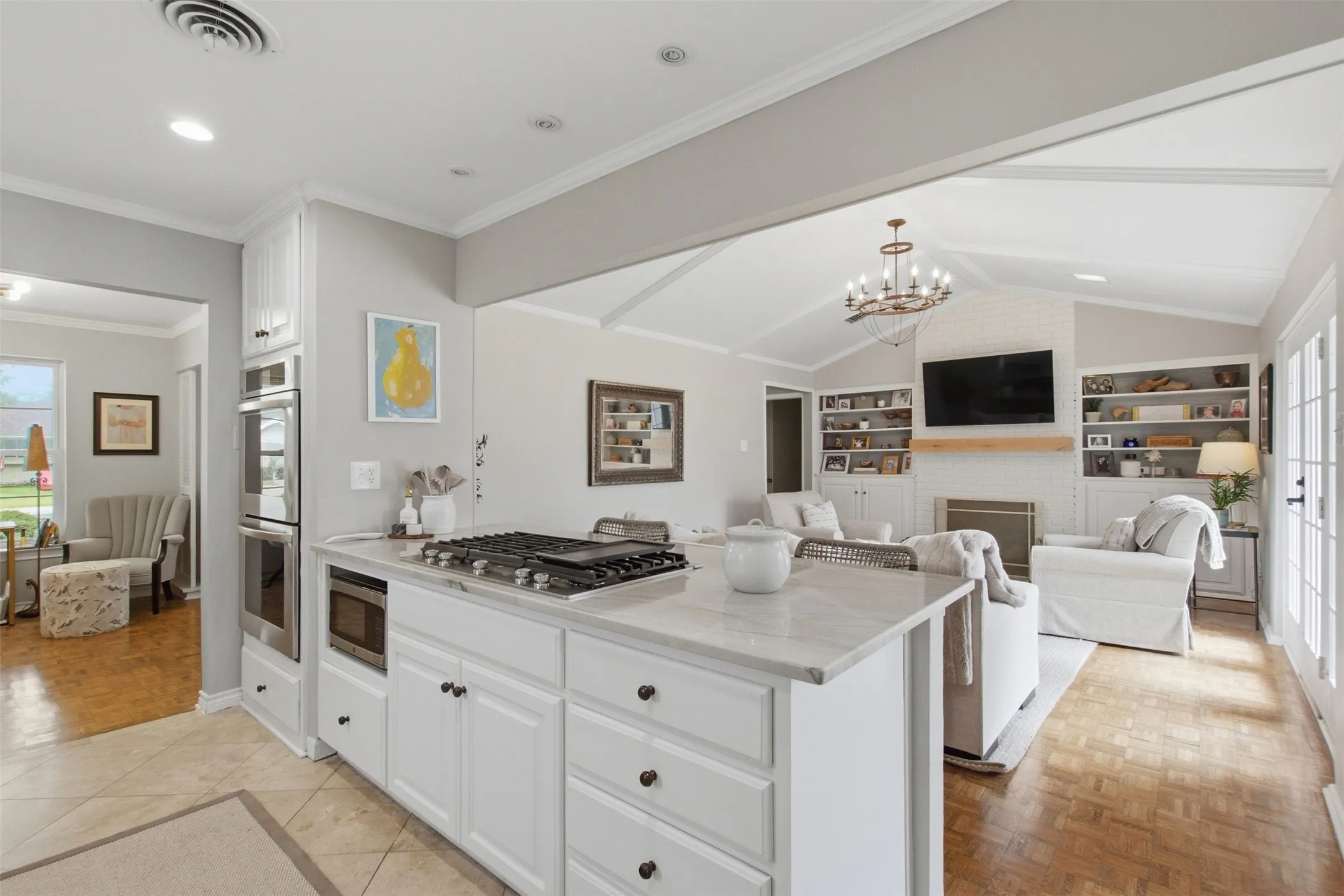 Kitchen island with integrated gas cooktop and white cabinetry, double wall ovens, vaulted ceiling, built-in shelving, and French doors