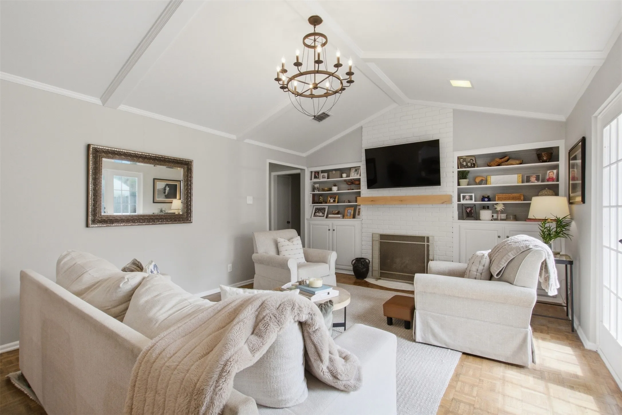 Vaulted ceiling with exposed beams, brick-surround fireplace with wood mantel, built-in shelving, wood-finish flooring, and French doors