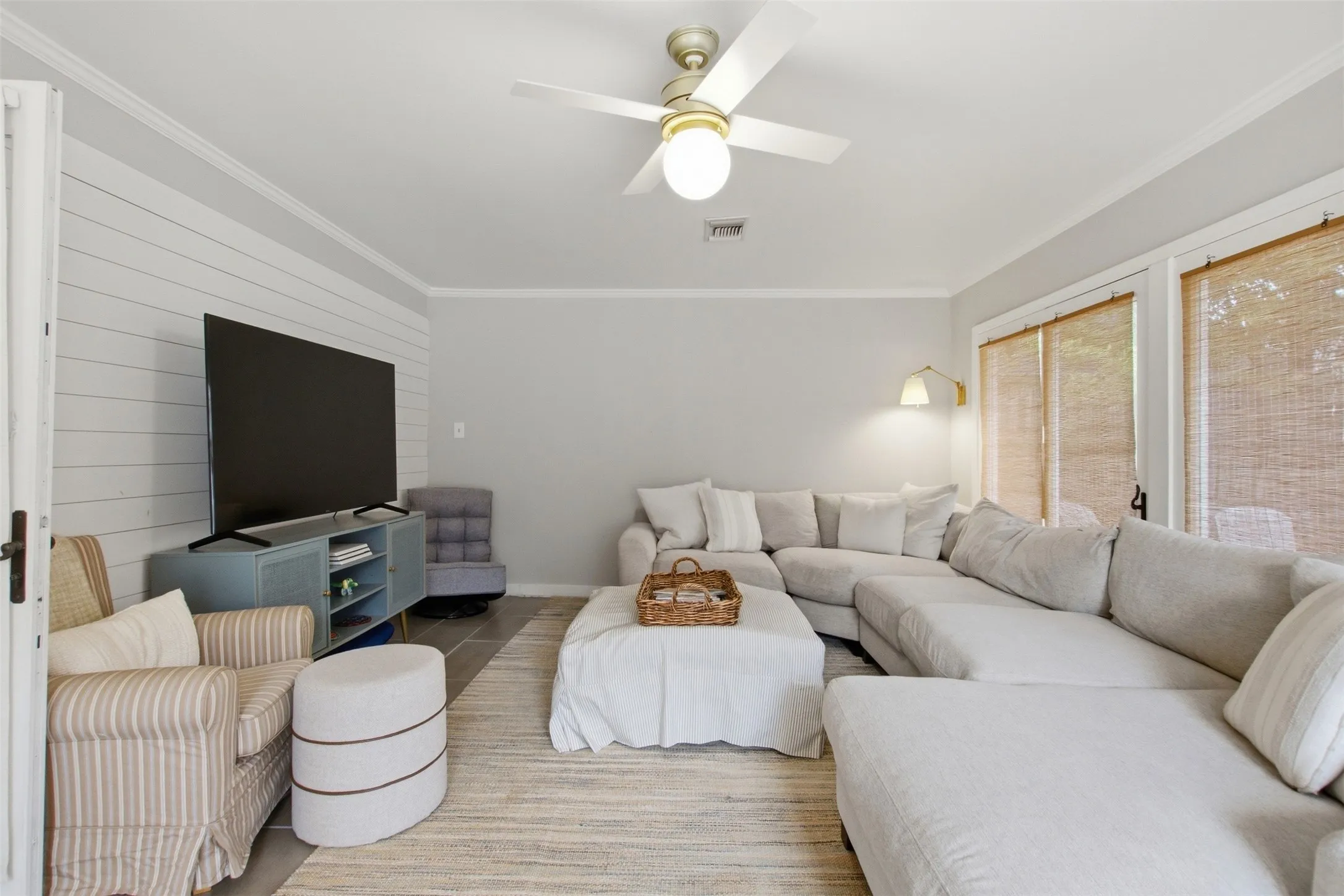 Shiplap accent wall, crown molding, ceiling fan with integrated lighting, wood-finish flooring, and multiple windows with woven shades
