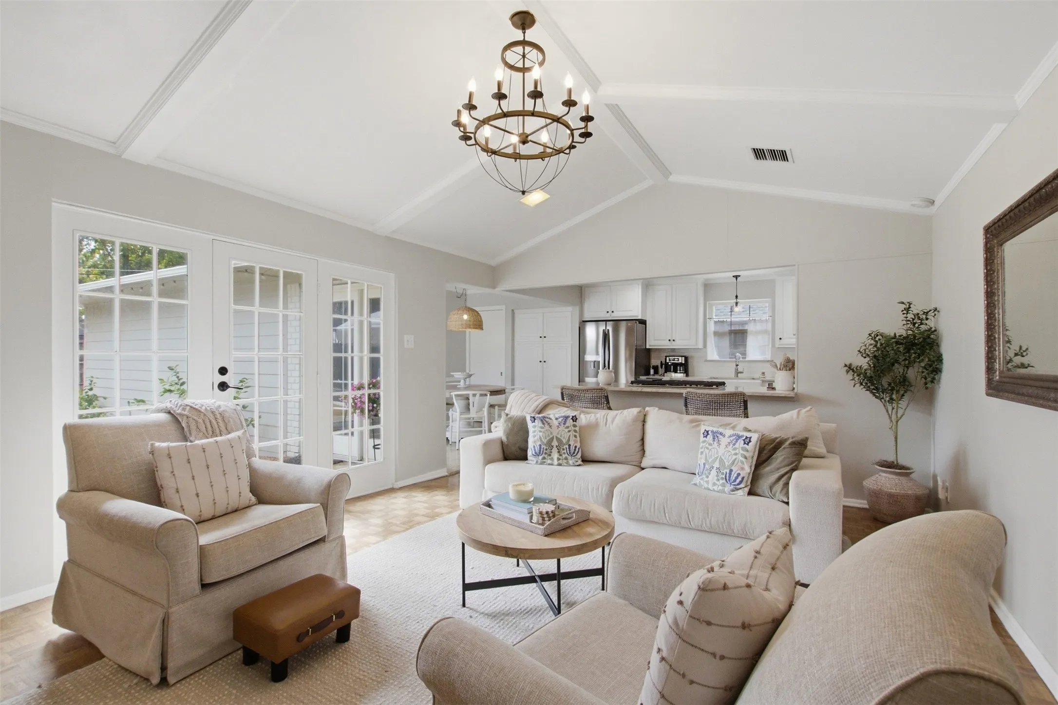 Vaulted ceiling with exposed beams, decorative chandelier, wood-finish flooring, white French doors, and a kitchen pass-through