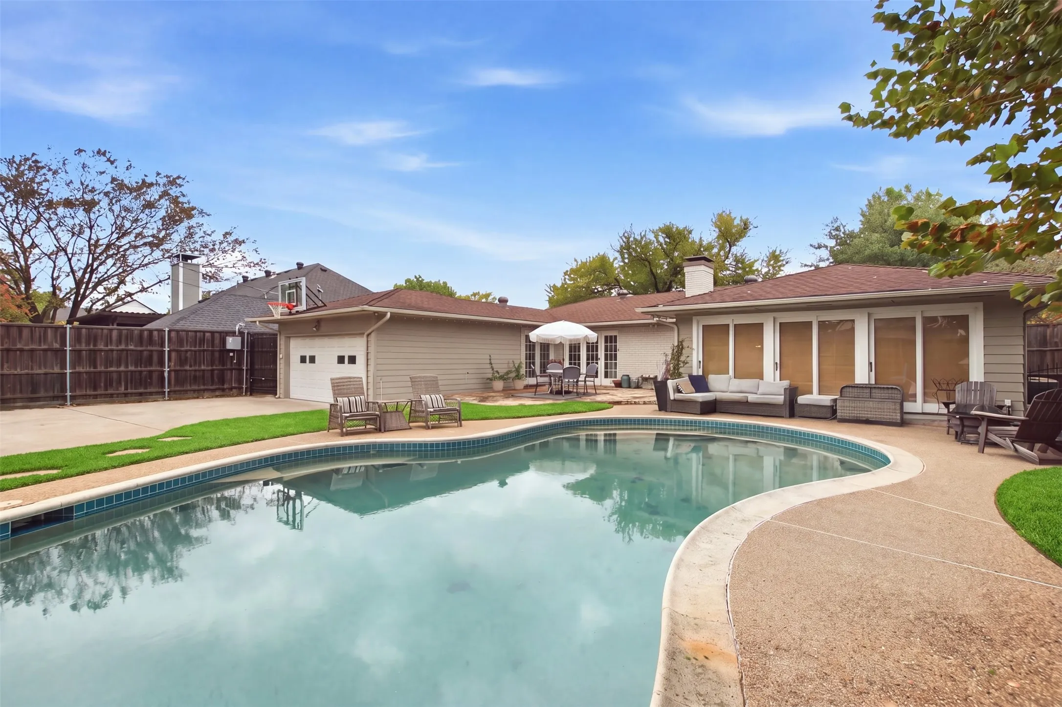 Resort-style backyard featuring a kidney-shaped pool, extensive concrete decking, and a detached two-car garage