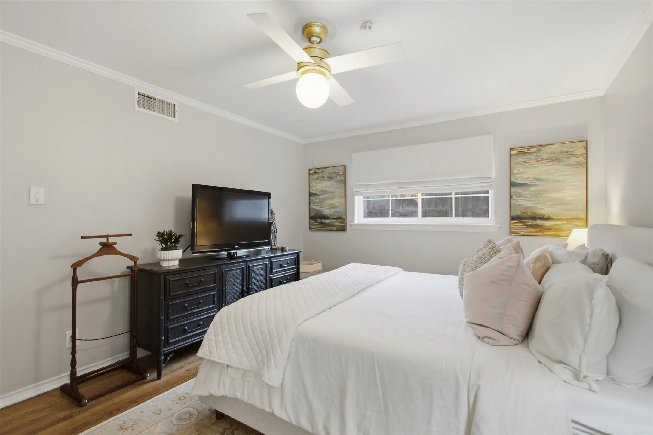 Hardwood-finish flooring, crown molding, ceiling fan, and window with white roman shade