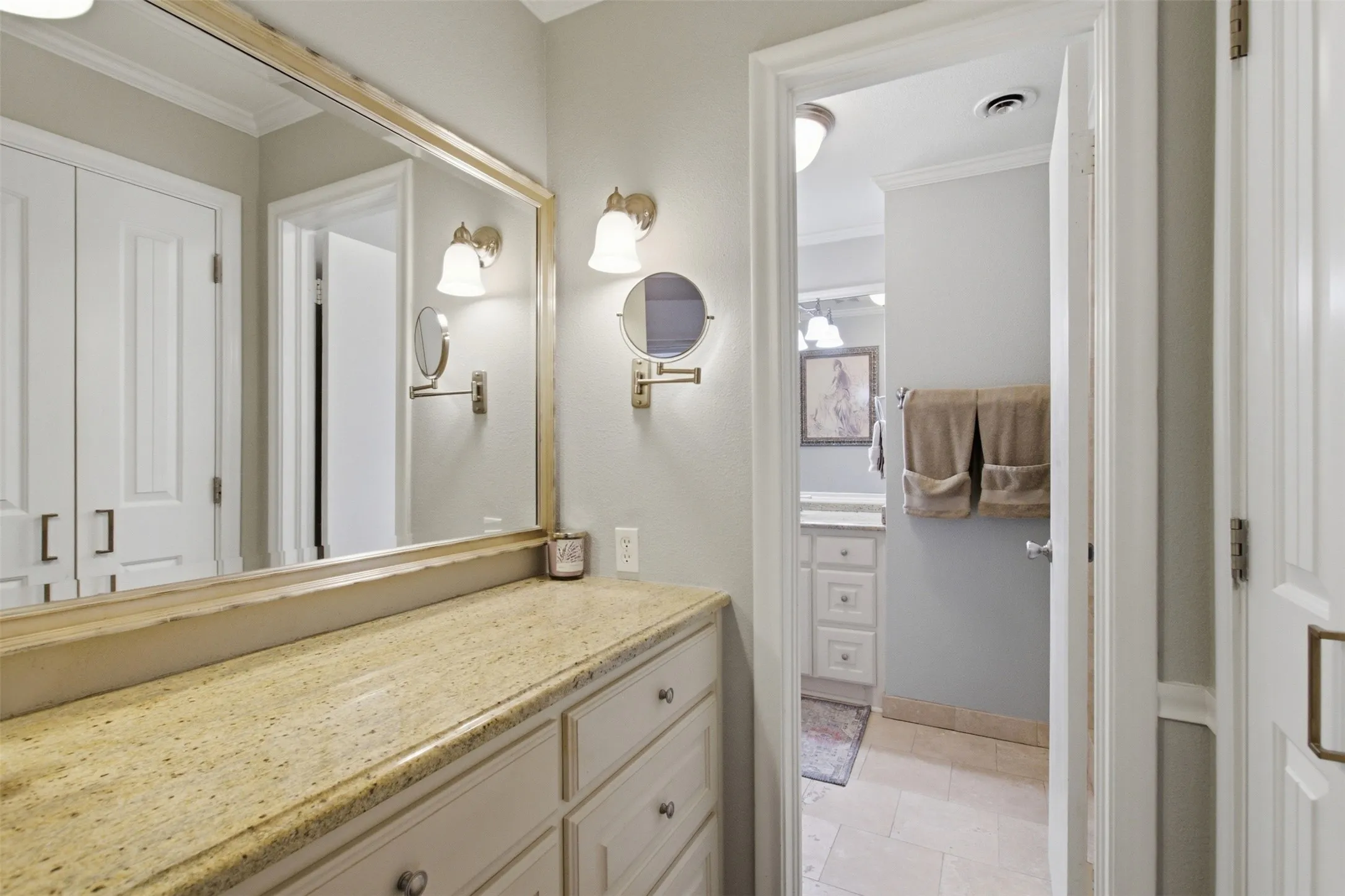 Built-in vanity with a stone countertop, custom cabinetry, large wall mirror, and dual wall sconces