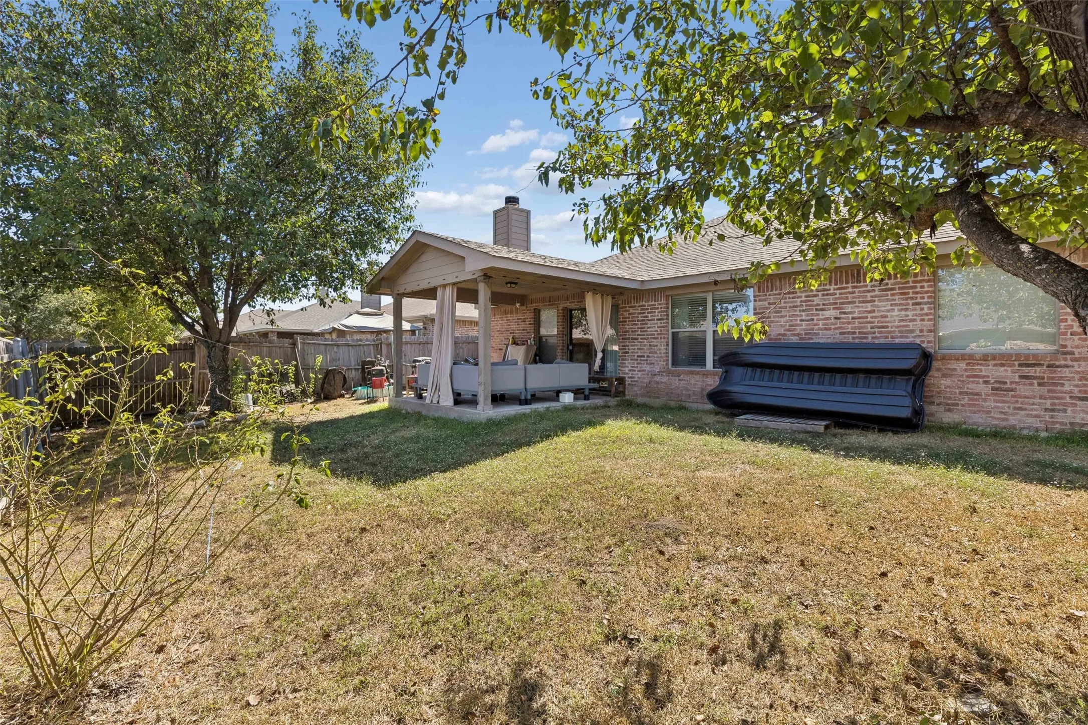 Expansive backyard featuring a covered patio, brick exterior, and mature trees