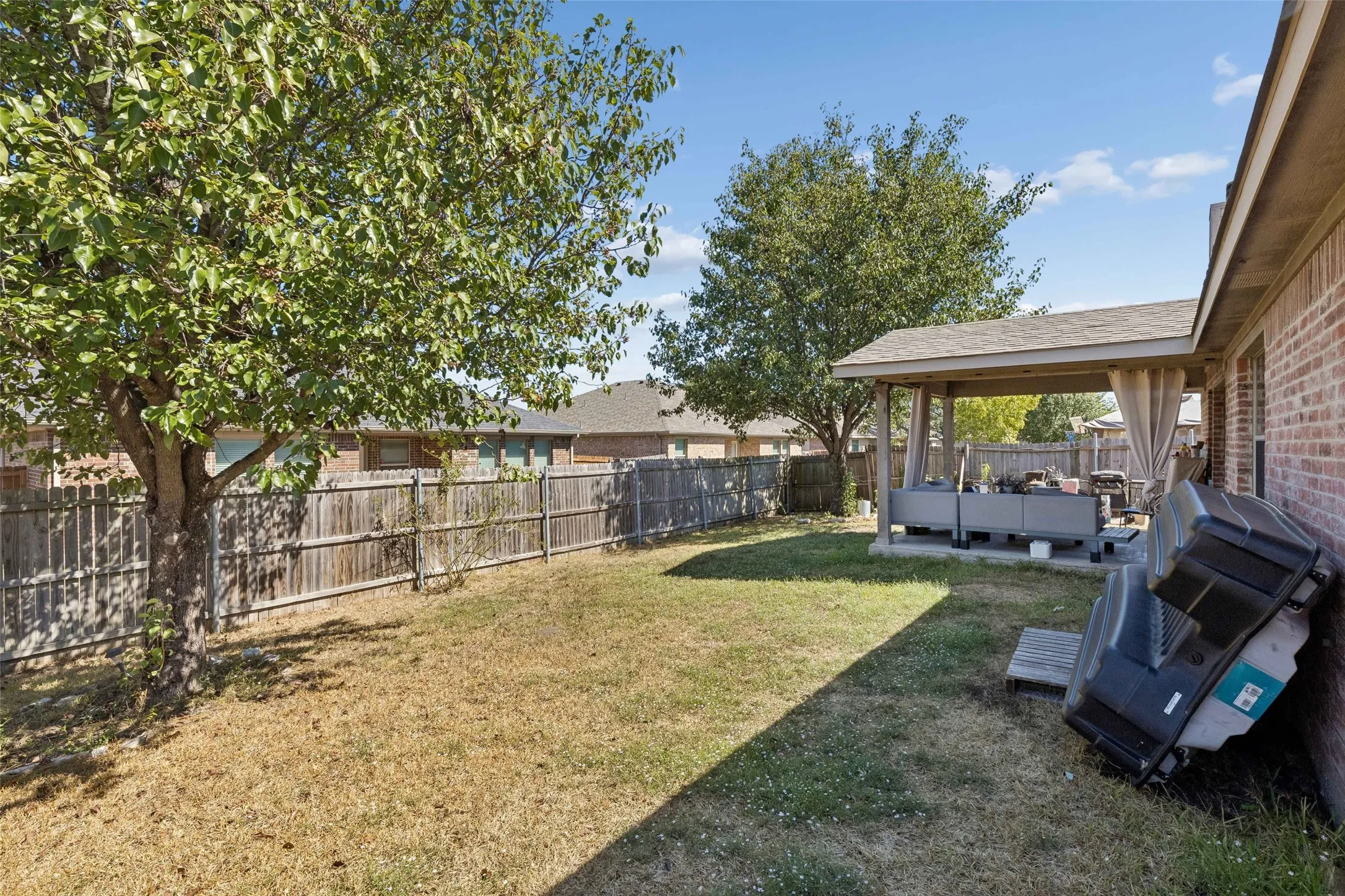 Expansive backyard featuring a covered patio, brick exterior, and a wooden privacy fence