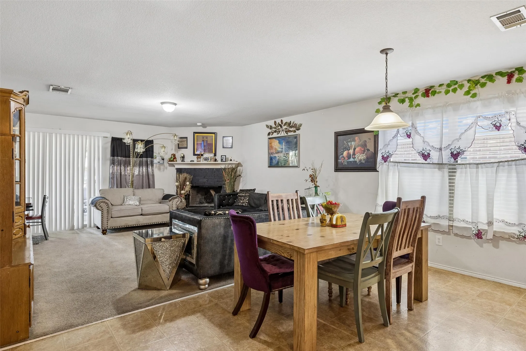 Combined living and dining area featuring a fireplace with a dark mantel, light-toned tile flooring, and a sliding glass door