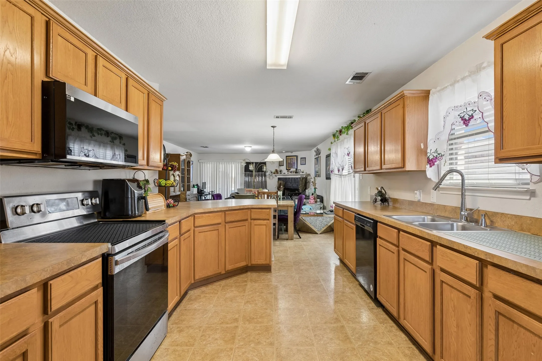 Kitchen featuring wood cabinetry, stainless steel appliances, a dual-basin sink, and tile flooring