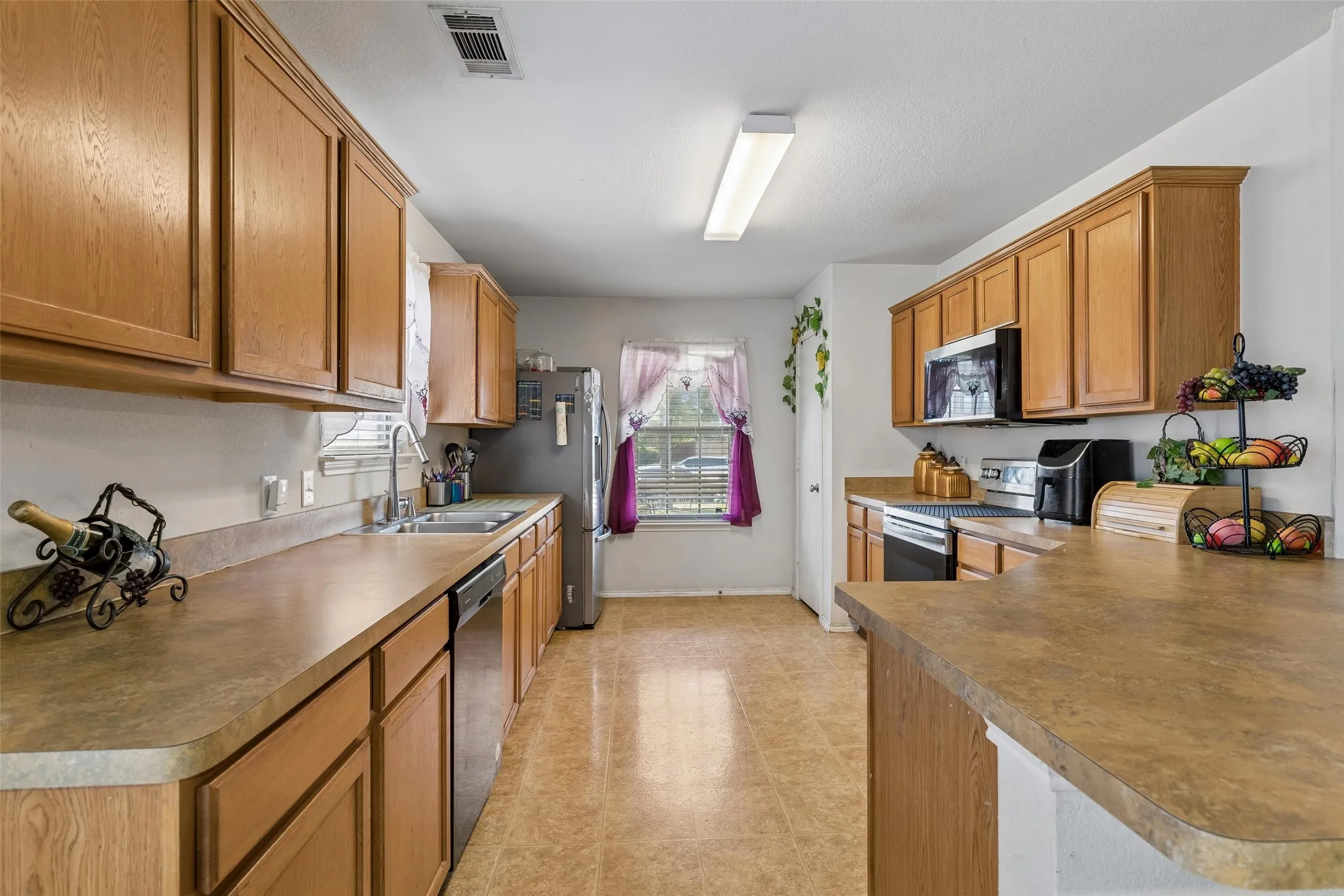 Wood-finish cabinetry, stainless steel appliances, dual basin sink, and a built-in microwave