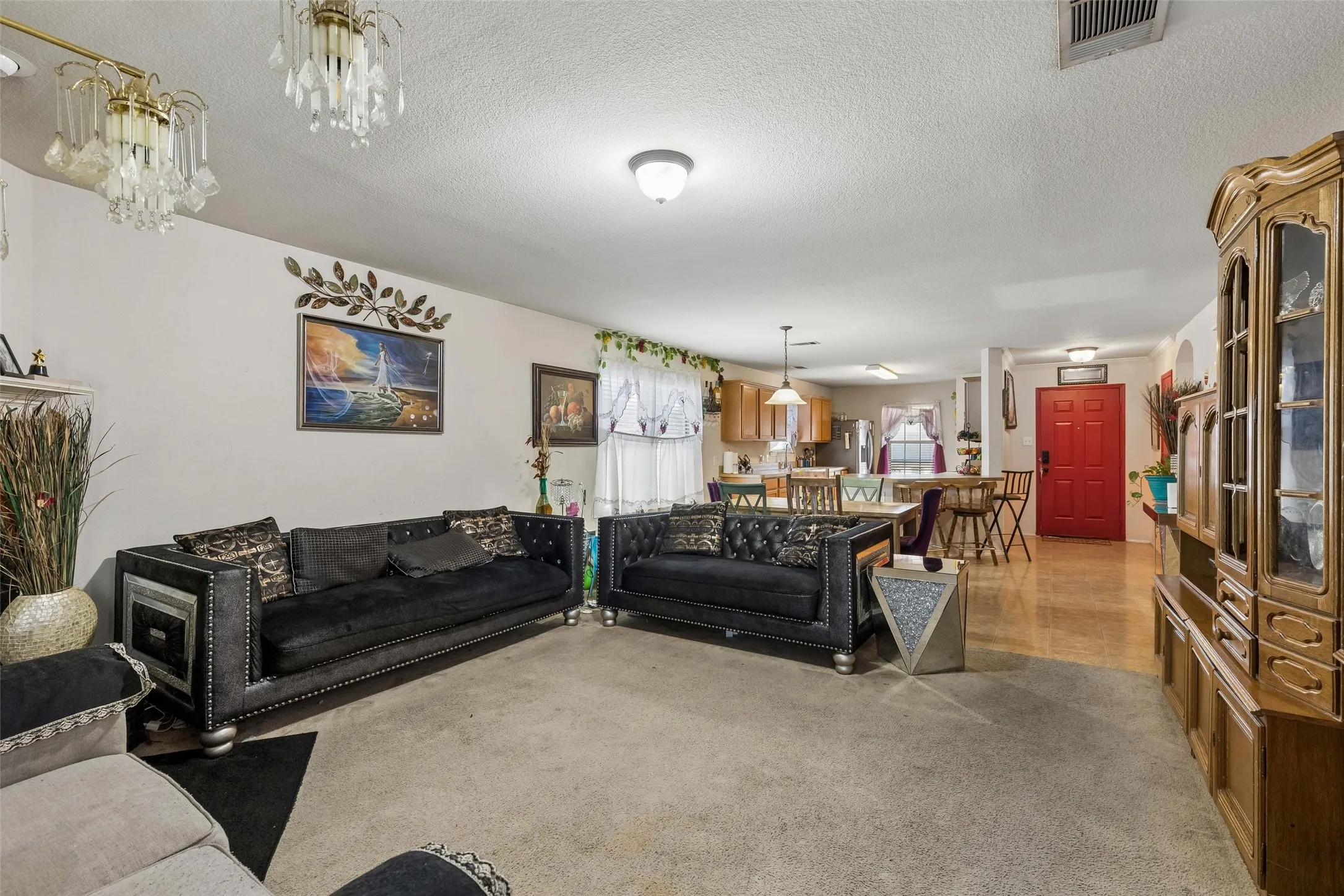 Open-concept living area featuring a red entry door, ceiling-mounted light fixtures, wood-finish flooring, and a kitchen area with wood cabinetry