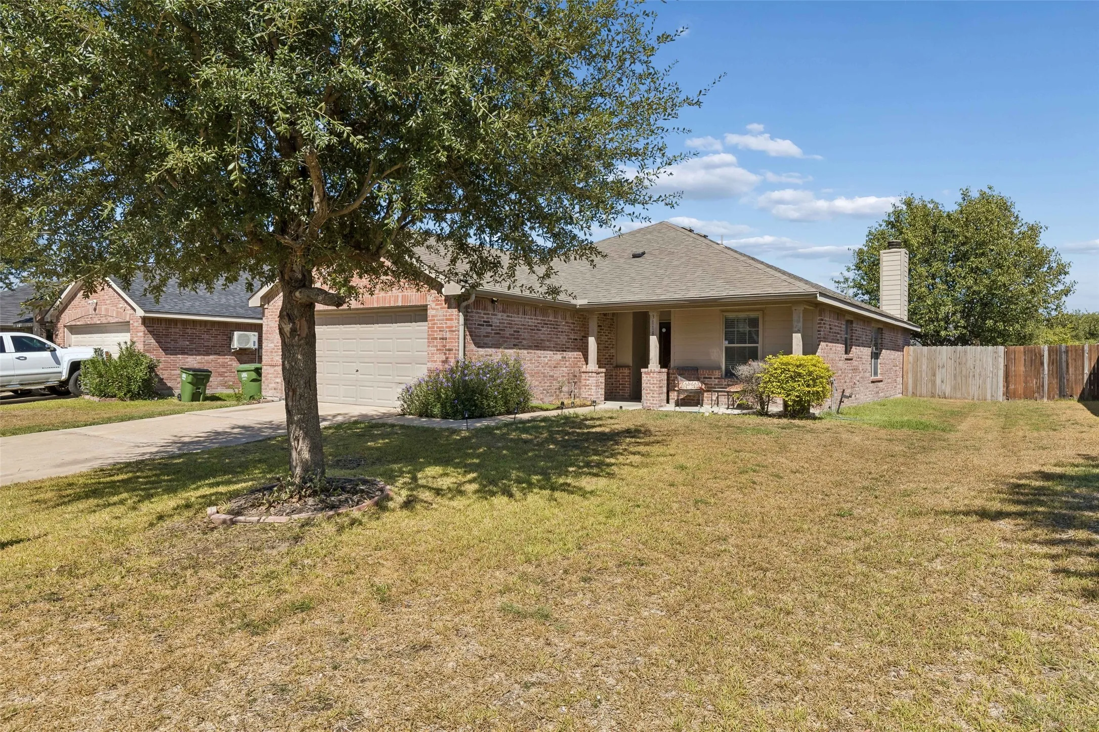 Brick exterior with covered front porch, attached garage, and mature landscaping