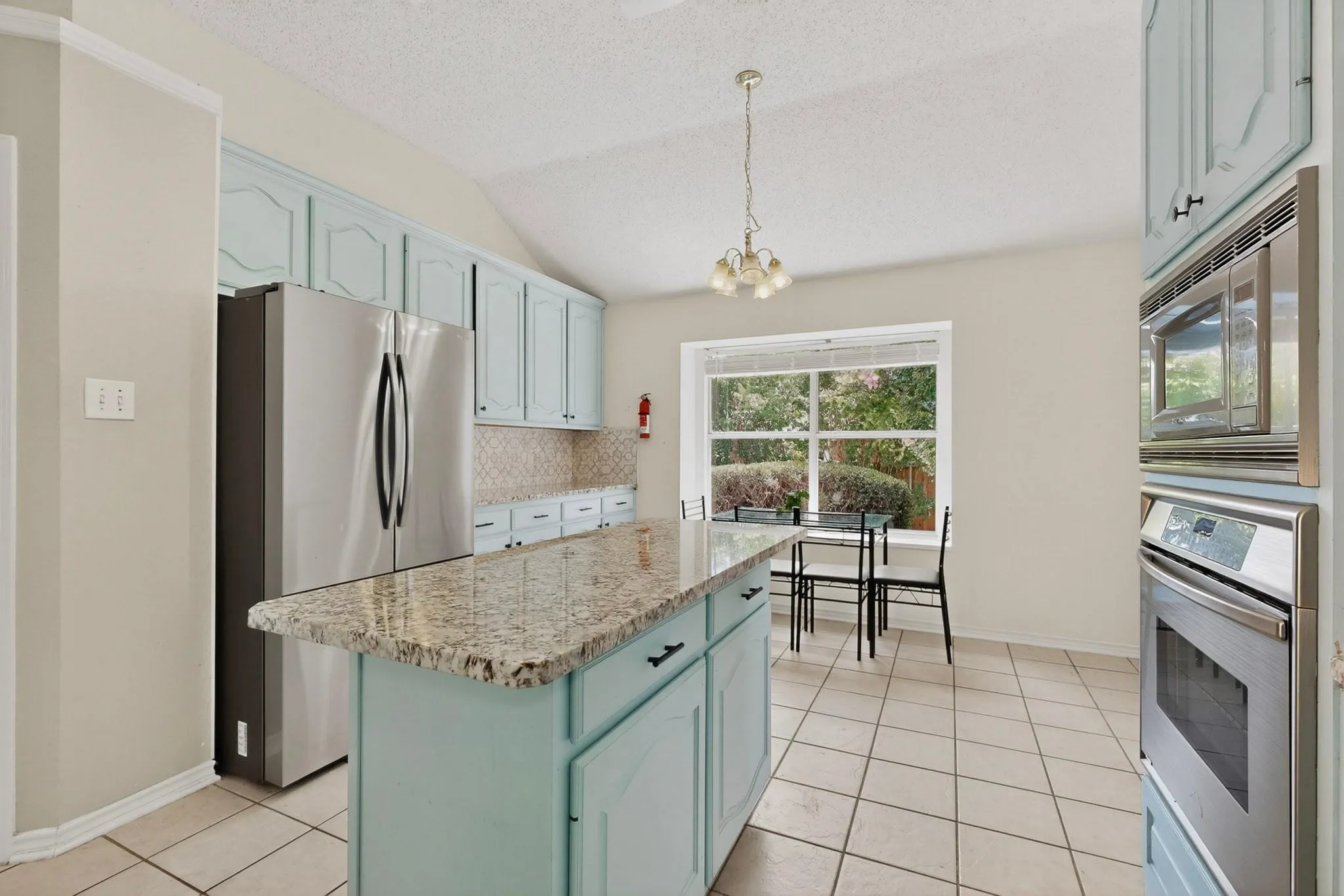 Kitchen featuring a central island with a speckled countertop, light blue cabinetry, tiled flooring, and a large window