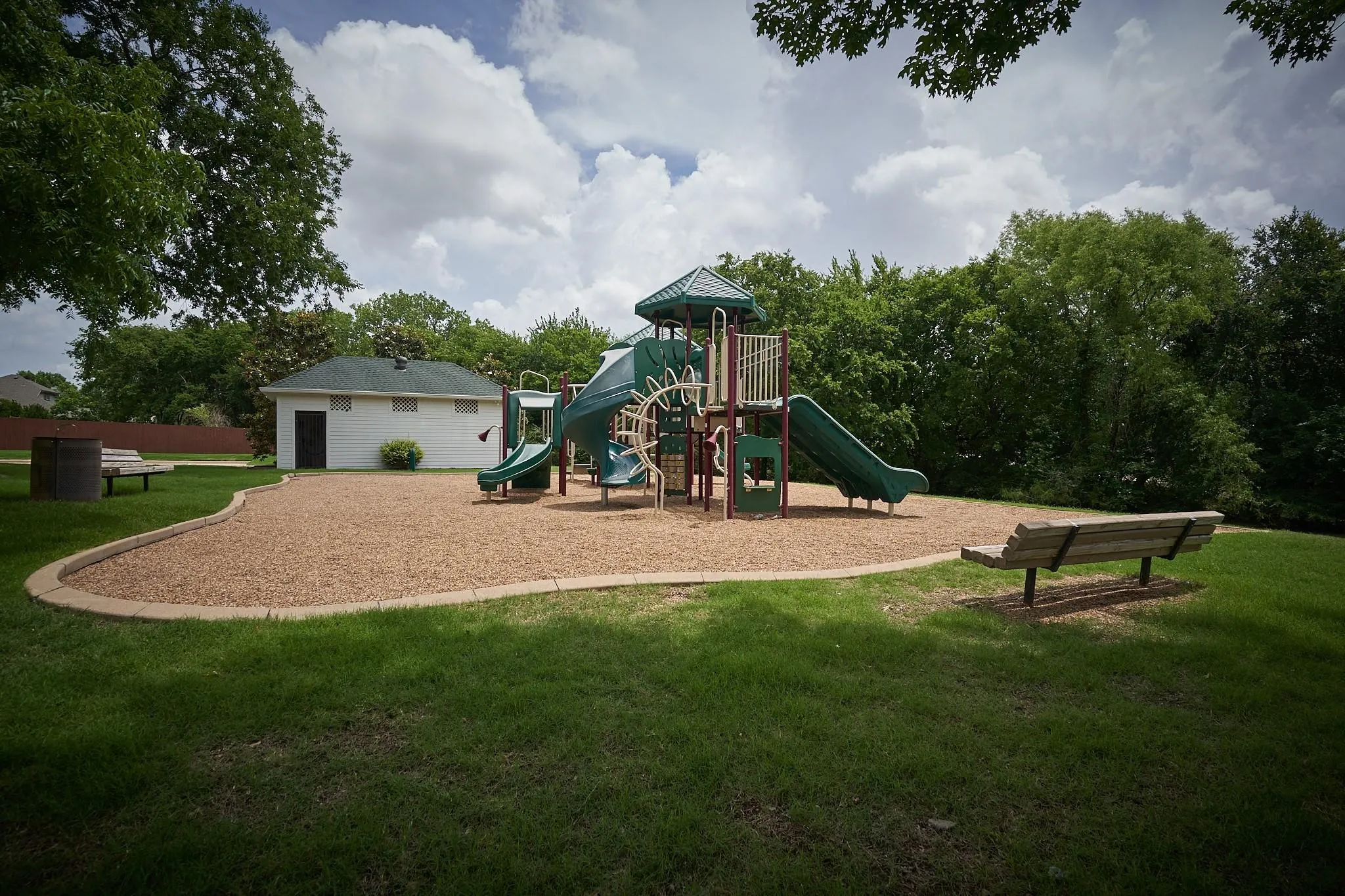 Expansive recreational area featuring a playground with slides, a manicured lawn, and mature trees