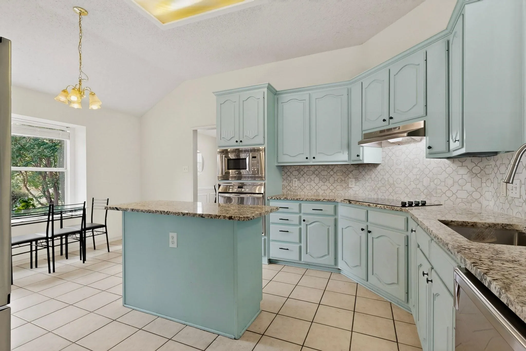 Kitchen featuring light blue cabinetry, granite countertops, tile backsplash, tile flooring, and vaulted ceiling