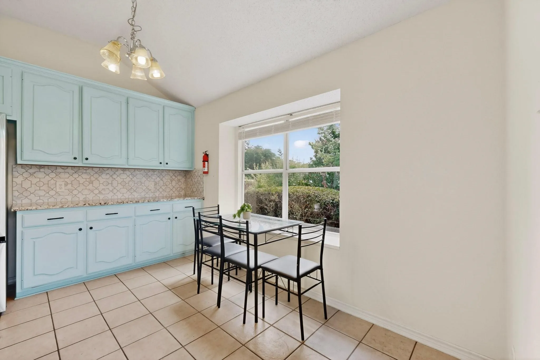 Kitchen with tile flooring, light blue cabinetry, patterned tile backsplash, and a window with blinds