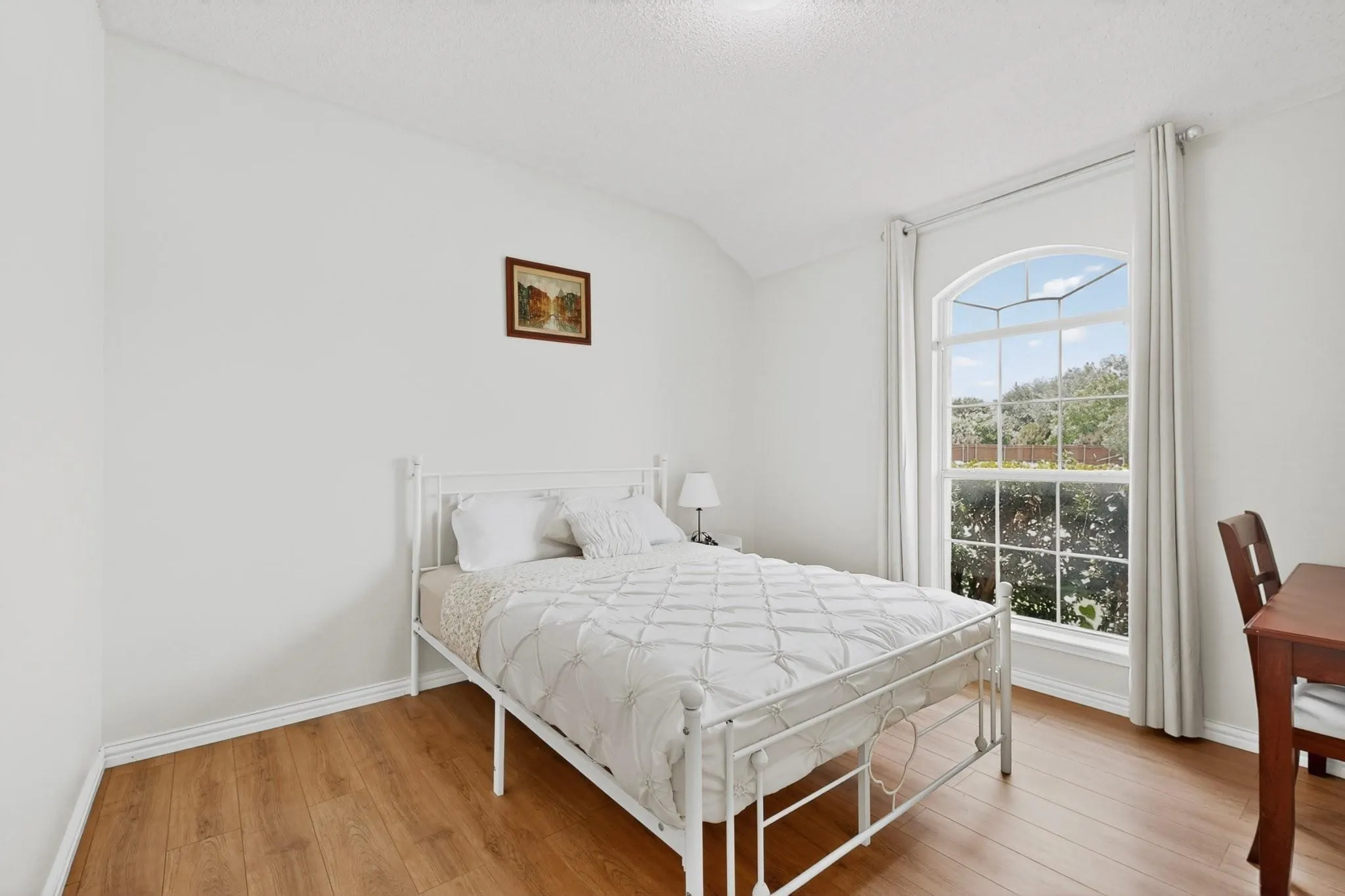 Wood-finish flooring, white walls, vaulted ceiling, and an arched window