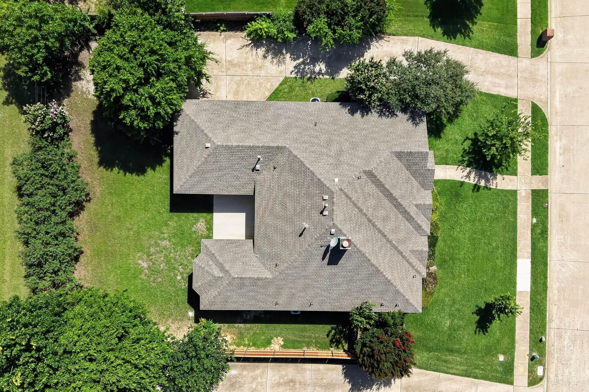 Pitched shingle roof with multiple gables, surrounded by expansive green lawn, mature trees, and concrete walkways