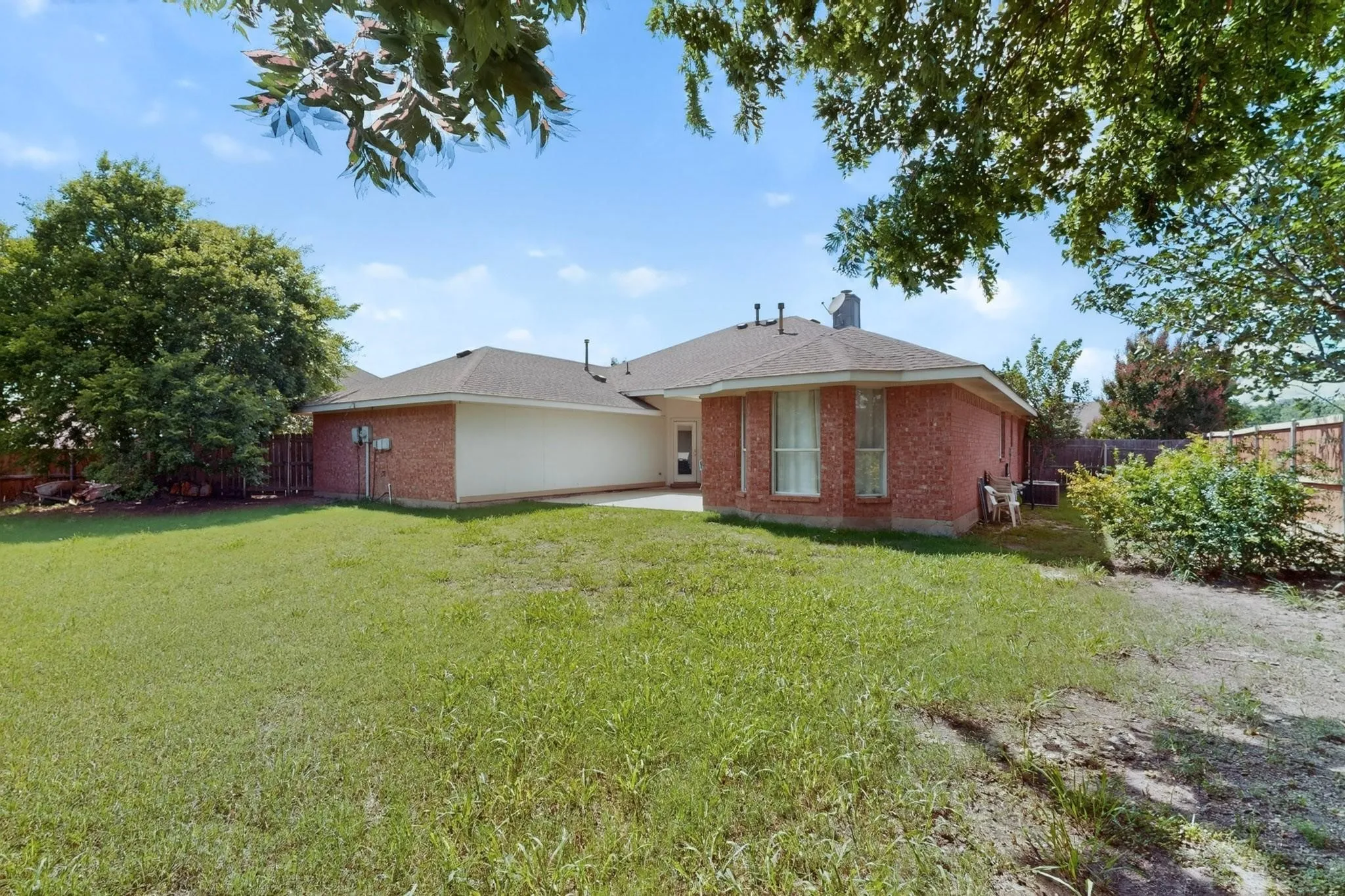 Expansive grassy yard with mature trees, brick exterior, and a private patio space