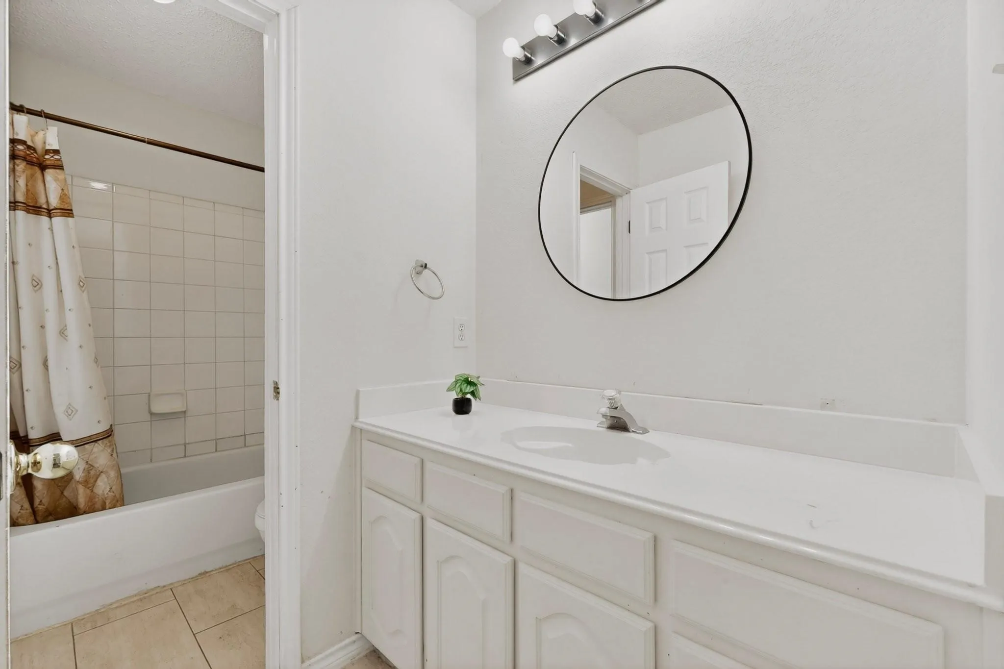 White vanity with a single basin sink, wall-mounted vanity lighting, and a circular mirror