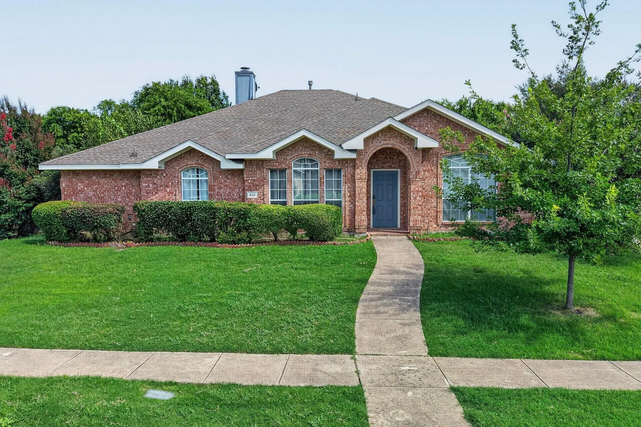 Brick exterior with arched entry, complementing gray door, and established landscaping