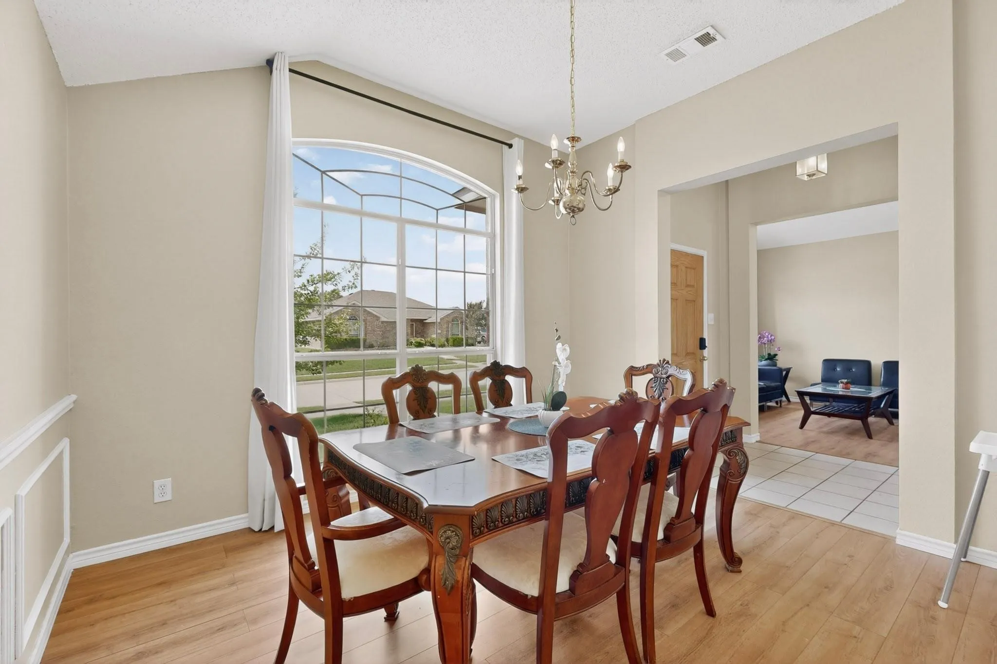 Formal dining space featuring wood-finish flooring, an arched picture window, wainscoting, and a brass-tone chandelier
