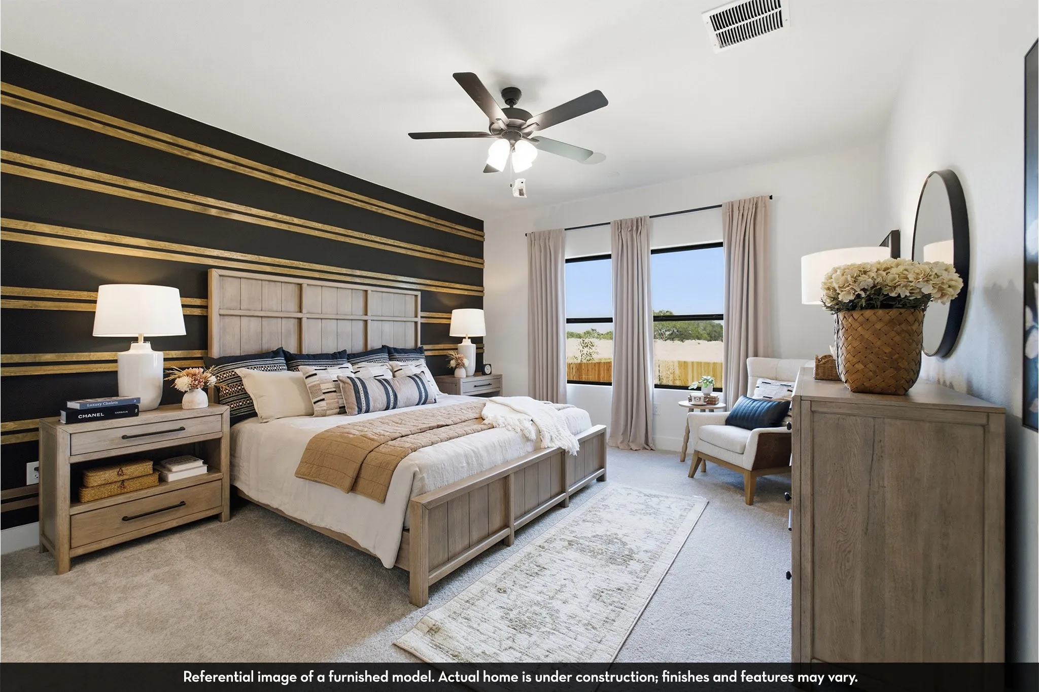 Accent wall with horizontal gold-striped detailing, ceiling fan with integrated lighting, three large windows, and wall-to-wall carpeting