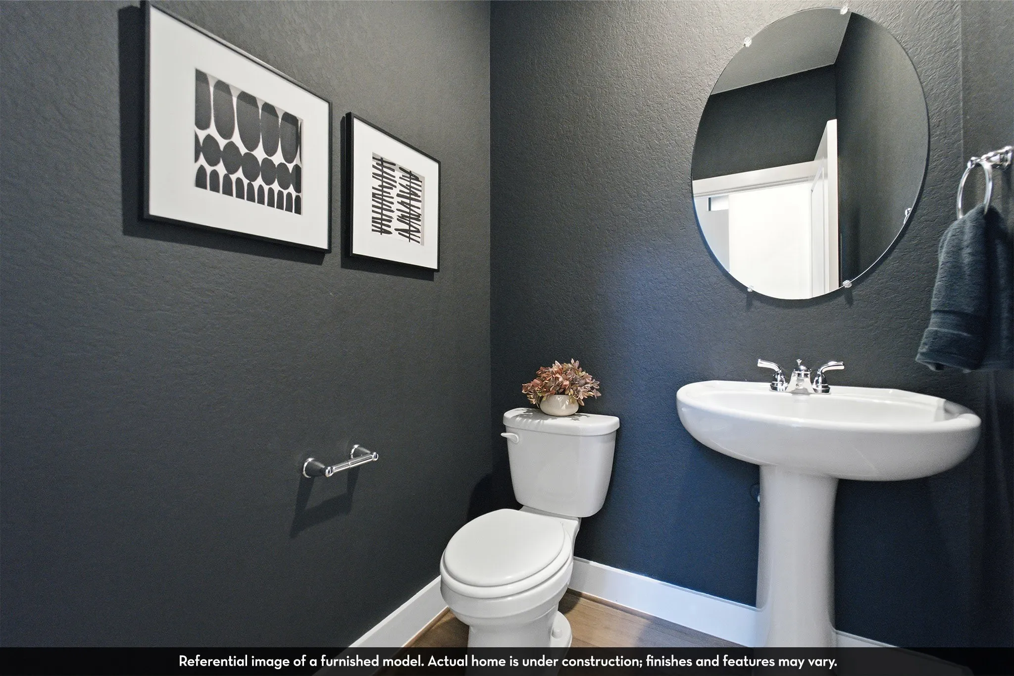Pedestal sink with chrome faucet, circular frameless mirror, and dark wall finish