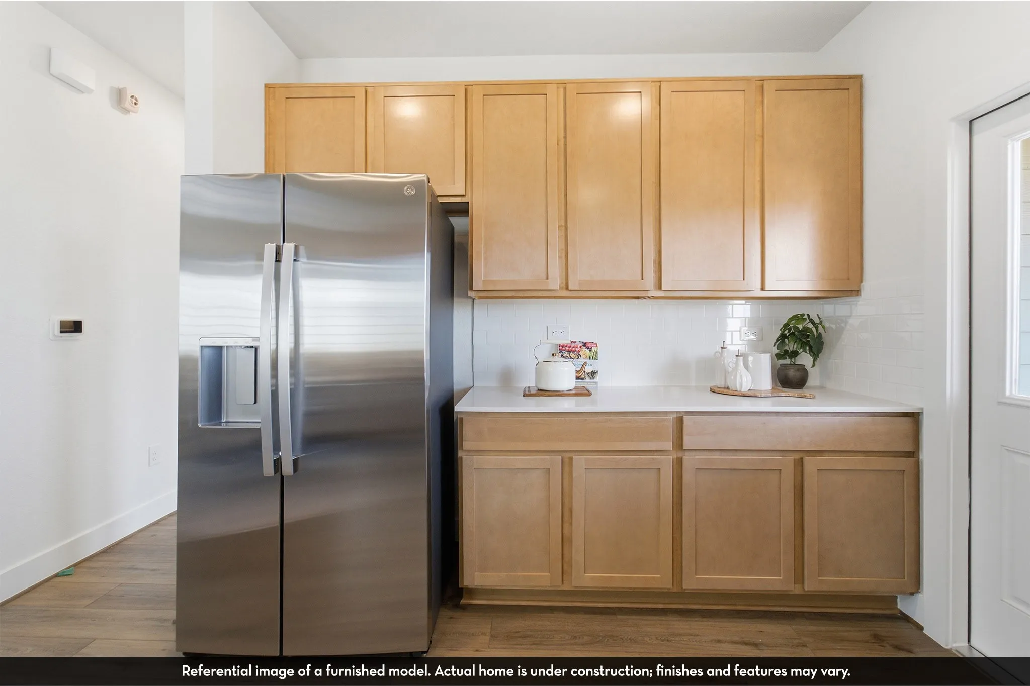 Light wood-finish cabinetry, white countertop, white subway tile backsplash, and wood-finish flooring