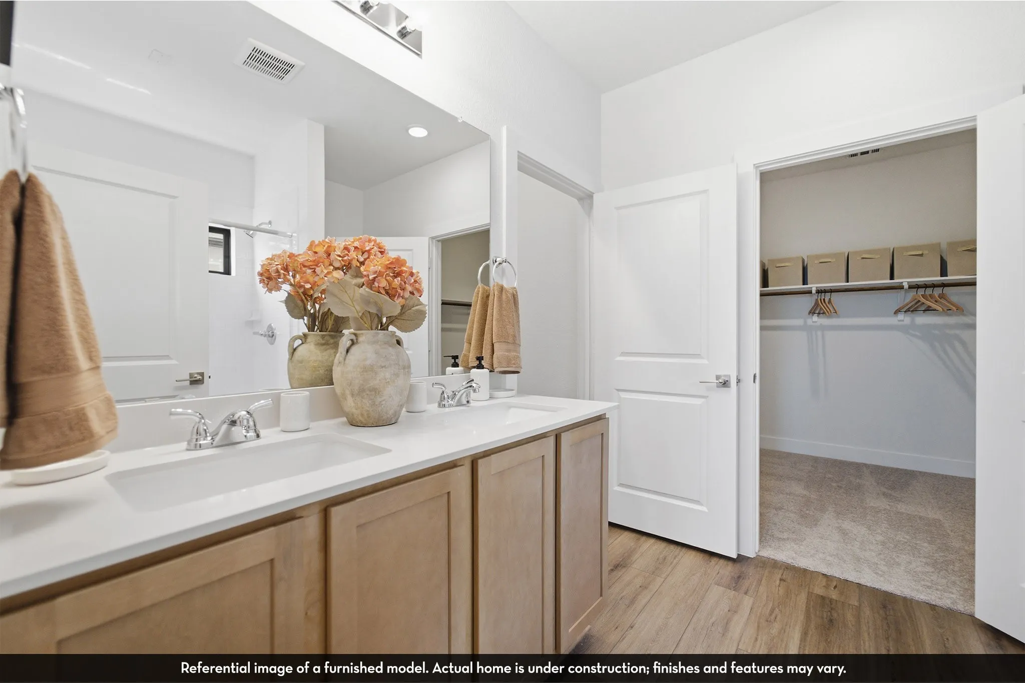 Double vanity with chrome faucets, wood-finish flooring, and a walk-in closet with shelving