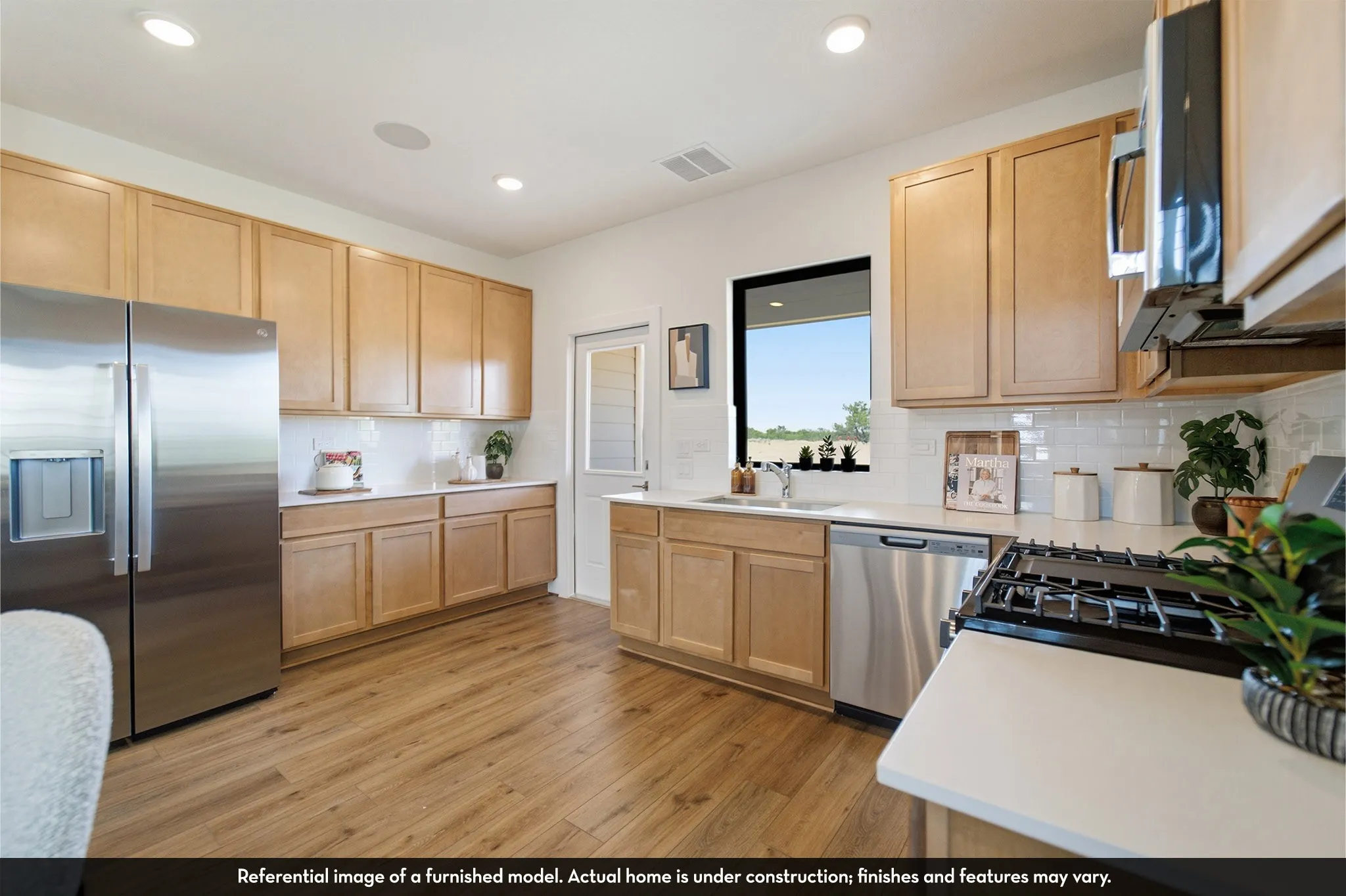 Kitchen featuring stainless steel appliances, light wood-finish cabinetry, white countertops, and wood-finish flooring