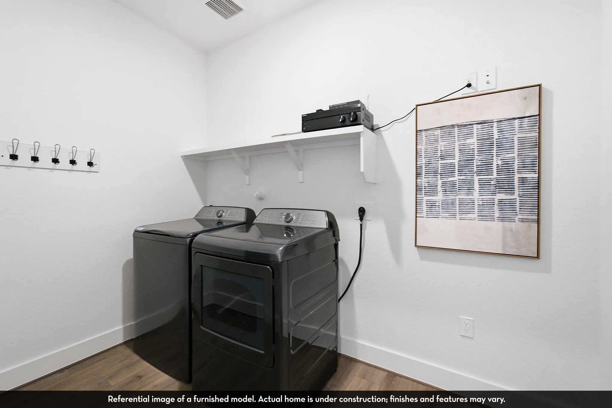 White laundry room featuring a wall-mounted shelving unit and wood-finish flooring
