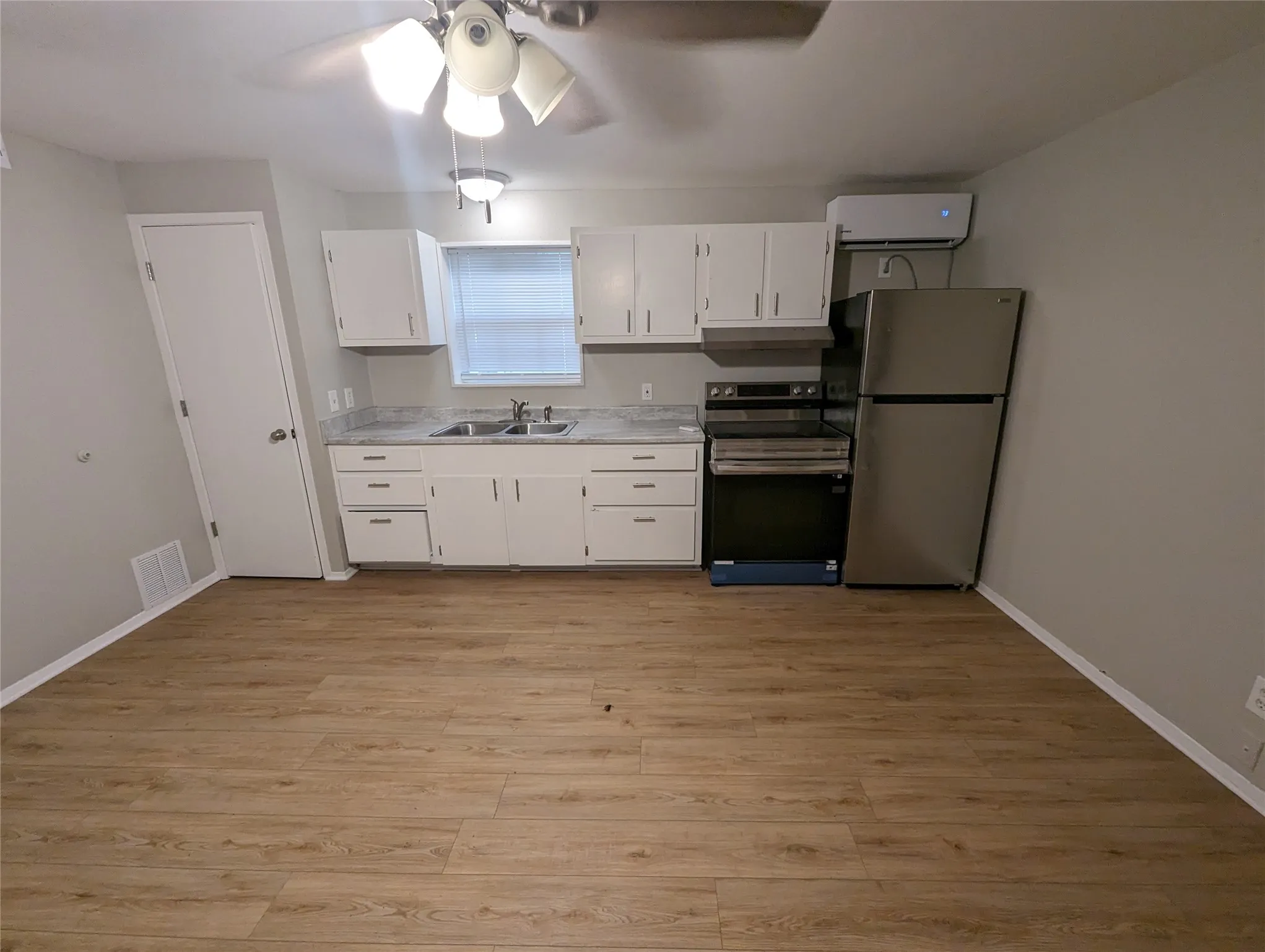 Wood-finish flooring throughout, white cabinetry, light countertops, stainless steel appliances, and a ceiling fan with integrated lighting