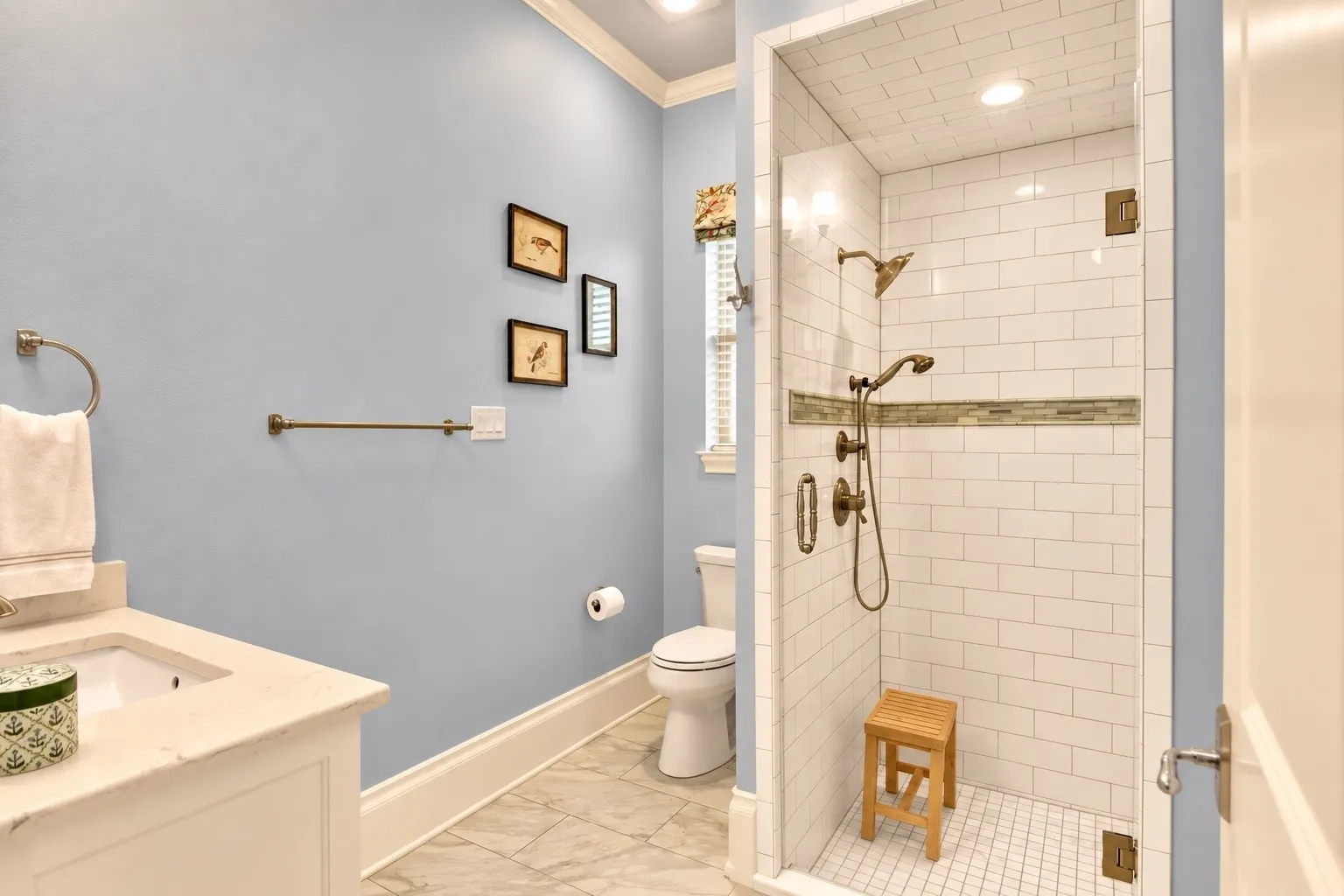 Tile flooring, single vanity with light-toned countertop, toilet, built-in shower with glass enclosure, white subway tile shower surround with accent band