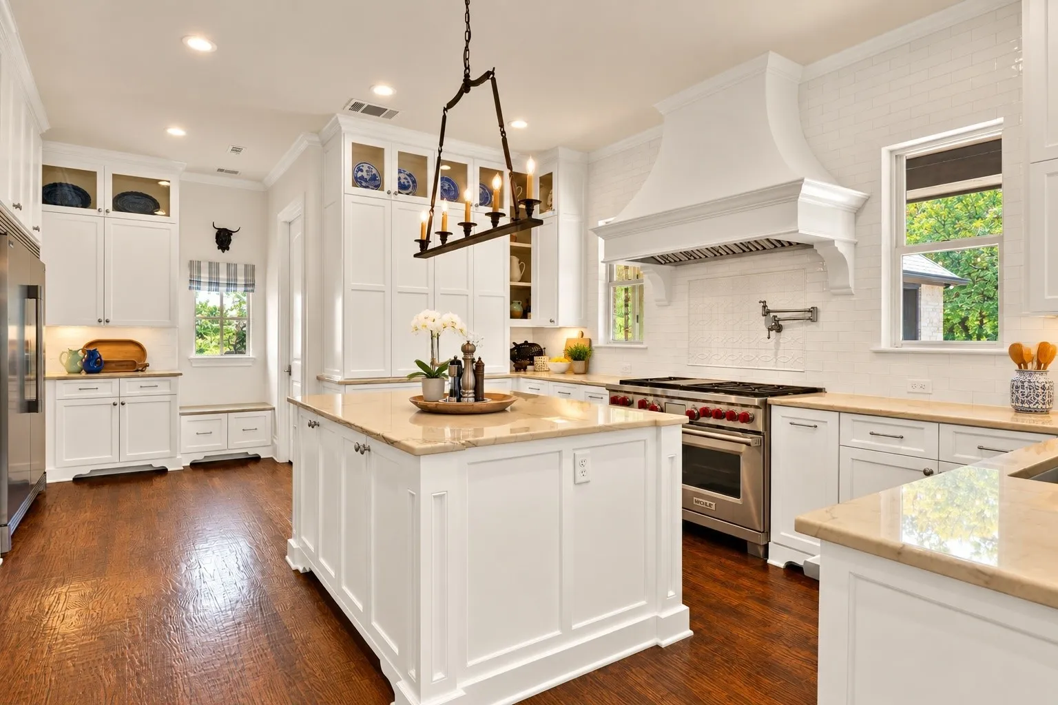 Gourmet kitchen with wood-finish flooring, white cabinetry, a large center island with stone countertop, stainless steel appliances, and a built-in window bench