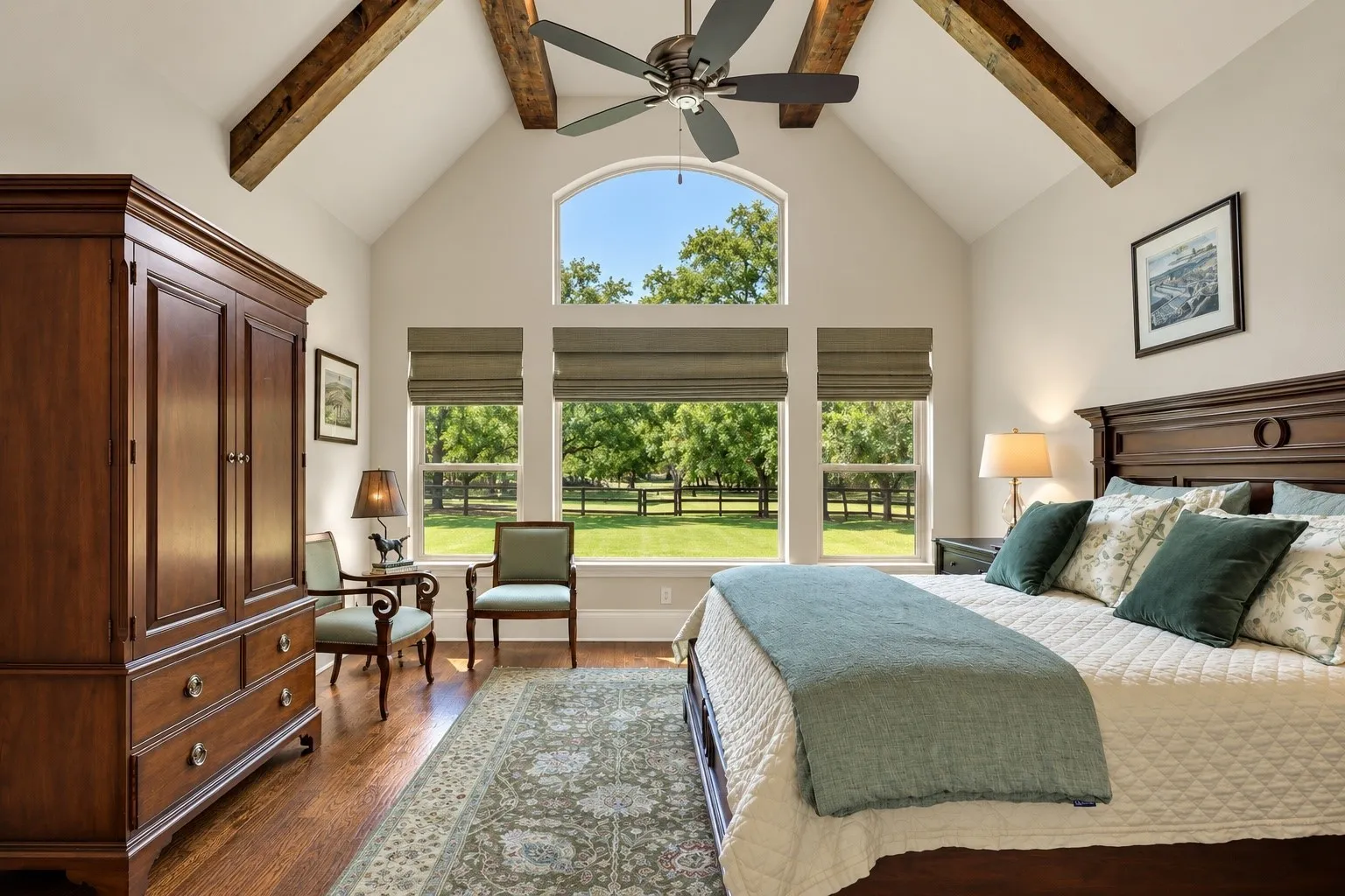 Vaulted ceiling with exposed wood beams, large arched window, multiple rectangular windows with blinds, wood-finish flooring, and a ceiling fan