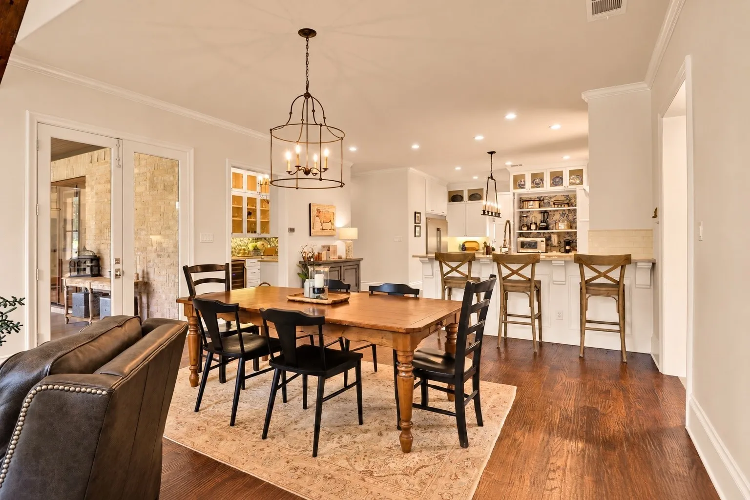 Hardwood flooring throughout, with a decorative ceiling light fixture, white crown molding, a built-in wet bar, and a kitchen island with seating