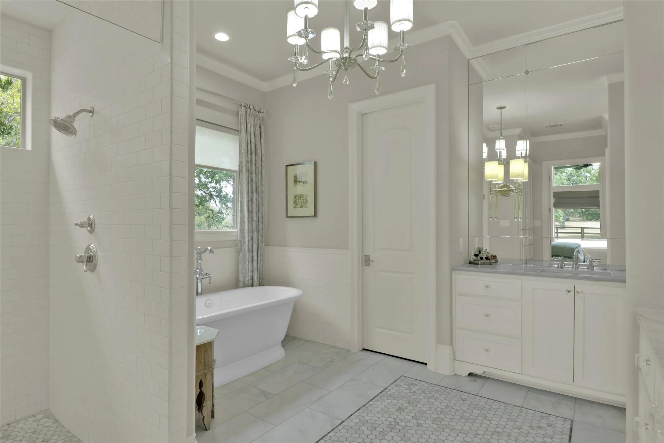 Freestanding soaking tub, walk-in shower with tile surround, double vanity with stone countertop, beveled mirror wall, and chandelier lighting
